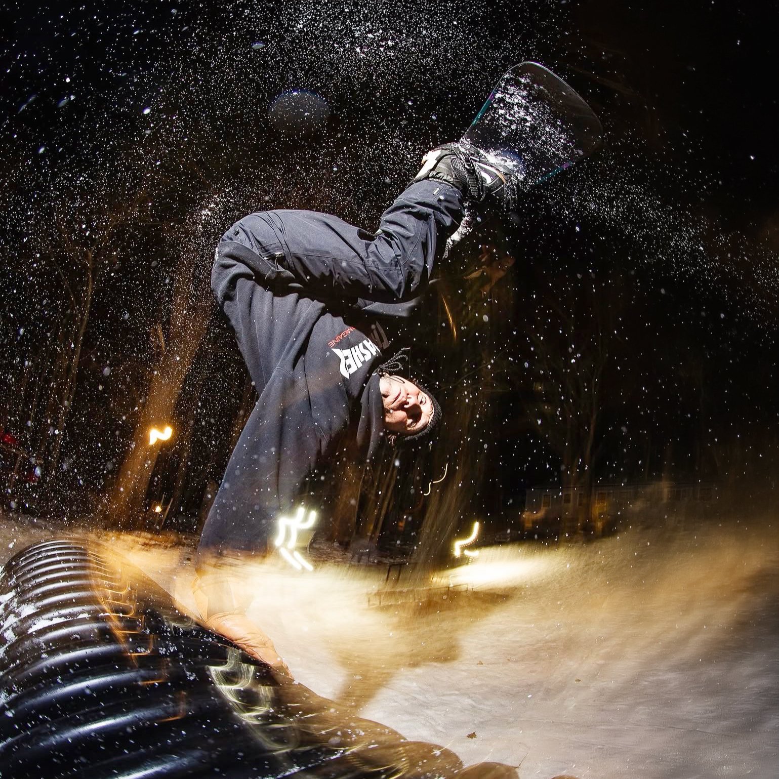 A person wearing a black hoodie and gray pants cleaning water with a squeegee during a rainy night.