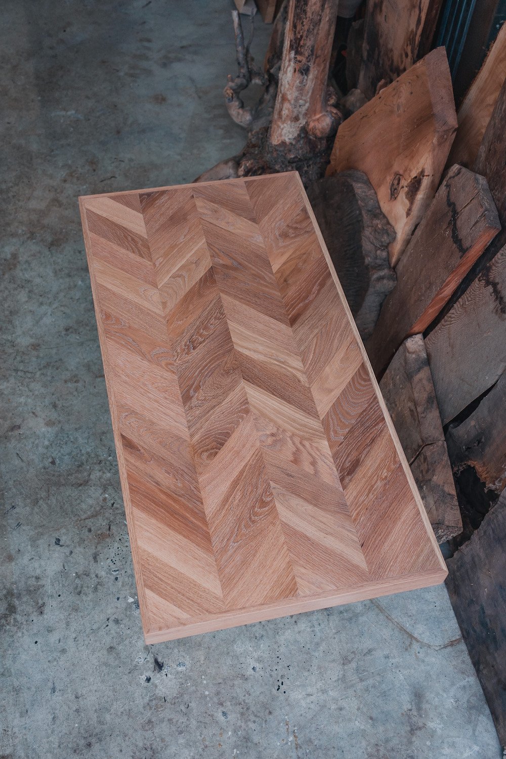 A wooden table with a herringbone pattern on top, placed on a concrete floor in a woodworking shop