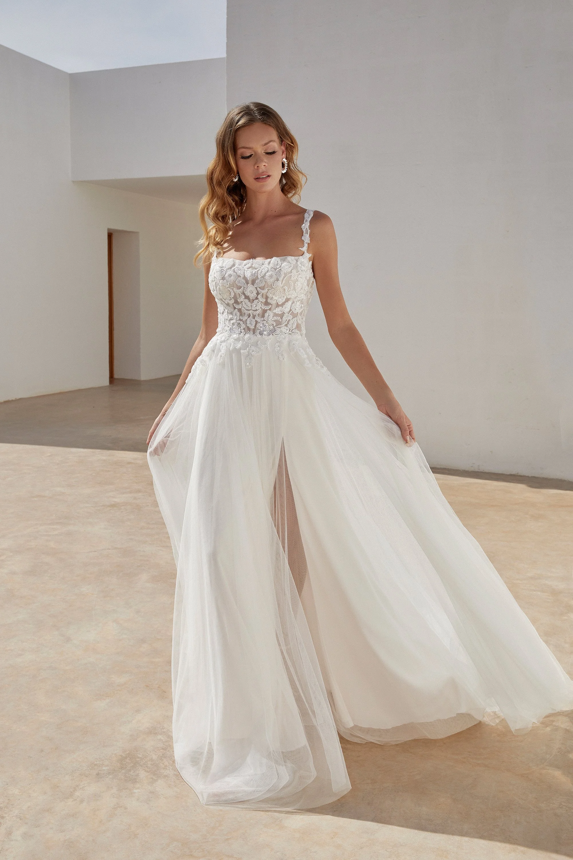 Frau in einem weißen Brautkleid mit Spitze und Tüll, stehende in einem hellen, minimalistischen Raum.