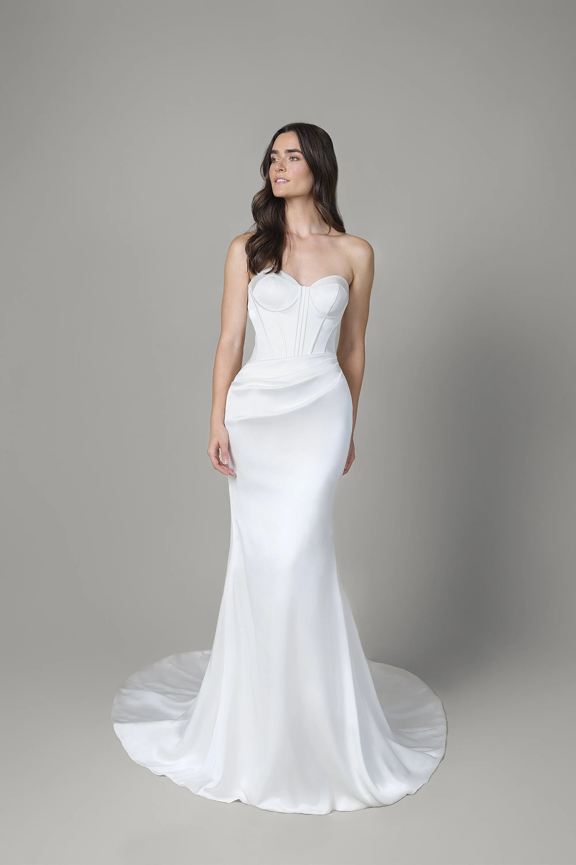 Frau in einem eleganten weißen Hochzeitskleid vor neutralem Hintergrund.