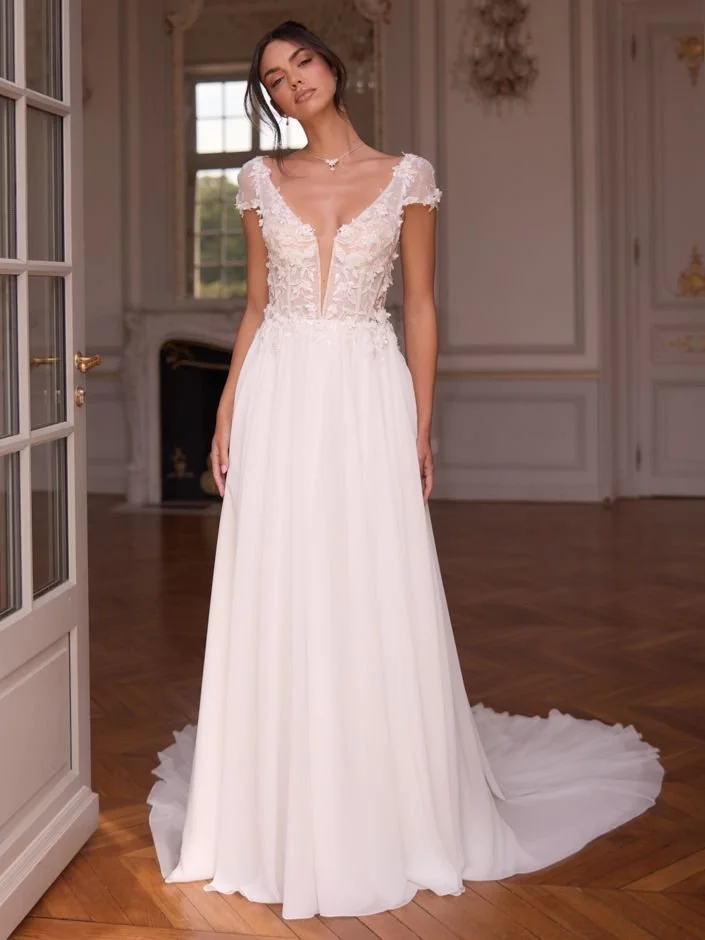 Eine Frau trägt ein elegantes, weißes Ensemble mit weitem Hosenanzug und lockerer Bluse, in einem warmen, minimalistischen Raum.