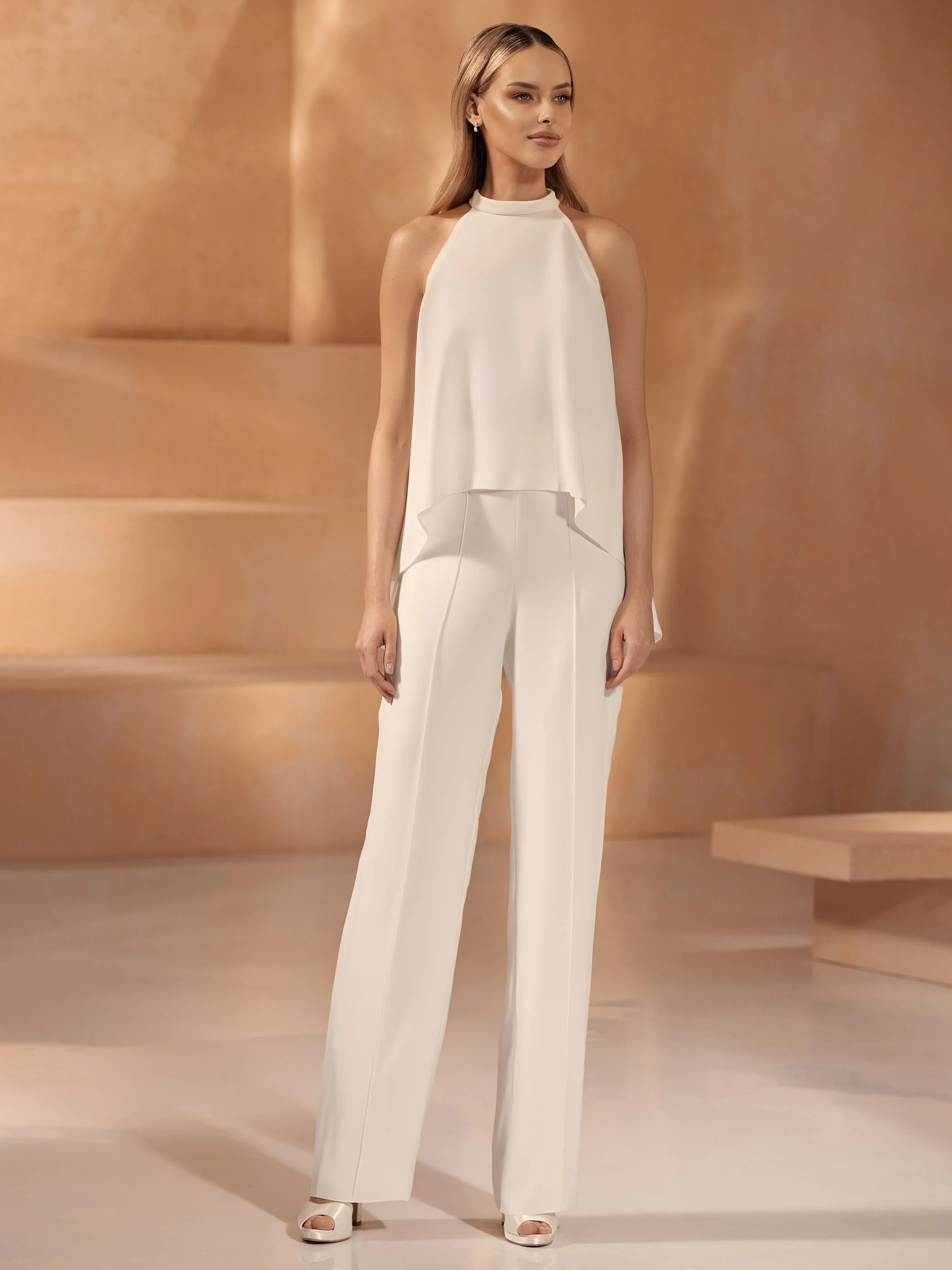 Eine Frau trägt ein elegantes, weißes Ensemble mit weitem Hosenanzug und lockerer Bluse, in einem warmen, minimalistischen Raum.