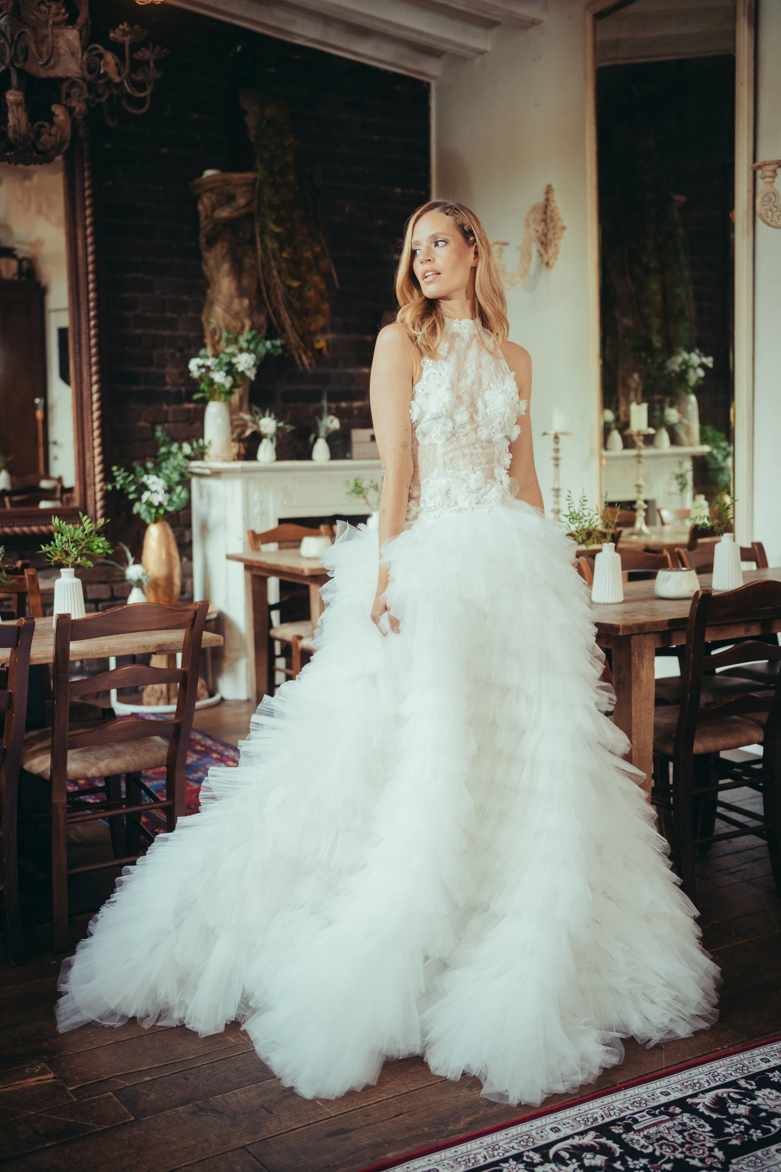 Frau in einem weißen, transparenten Abendkleid mit Blumendetails und hohen Beinen, stehend vor einem Bühnenvorhang.