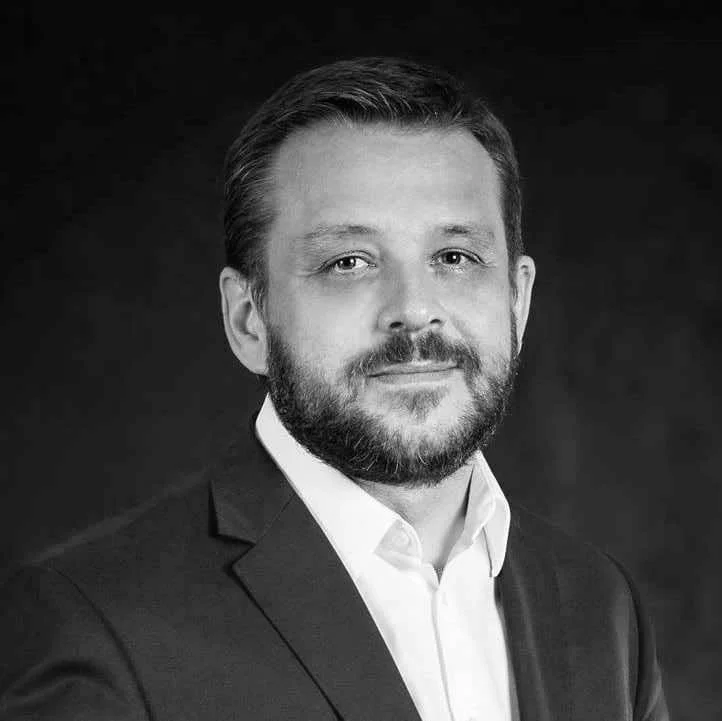 Black and white portrait of a man in a suit and white shirt, with short hair and a beard.