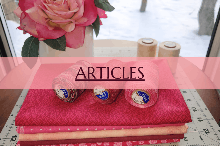 Spools of pink and red sewing thread on folded pink fabric, with a pink rose in a vase and two wooden spools in the background.