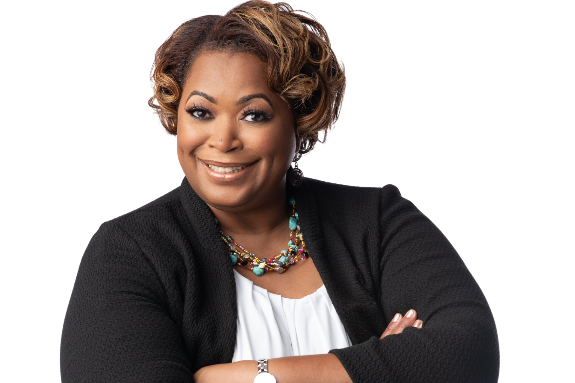 A smiling African-American woman with short curly hair, wearing a black blazer, white blouse, colorful layered necklaces, and earrings, standing with arms crossed against a white background.