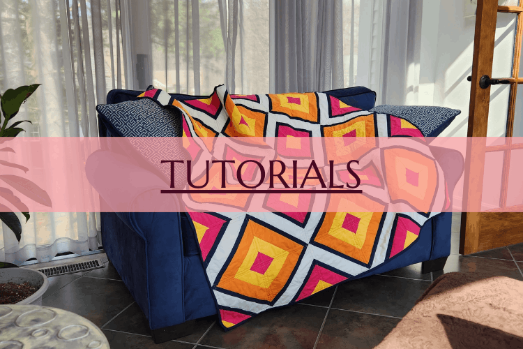 Blue couch with colorful geometric patterned blanket in a sunlit living room with large windows, curtains, potted plants, and a wooden door.