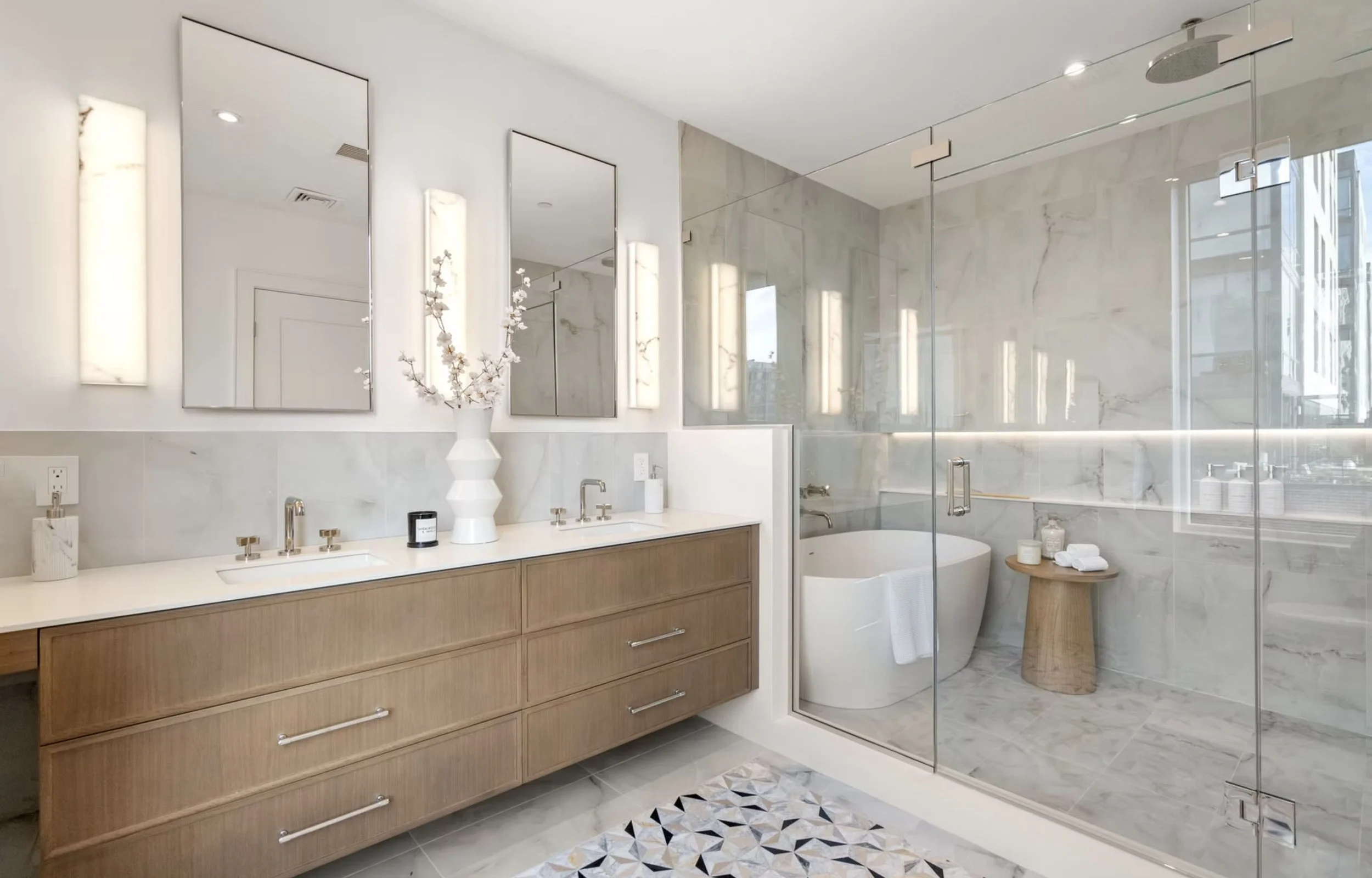 Modern bathroom with double vanity, large mirrors, white countertop, and a glass-enclosed shower and bathtub area, featuring marble walls and floor, and wooden accents.