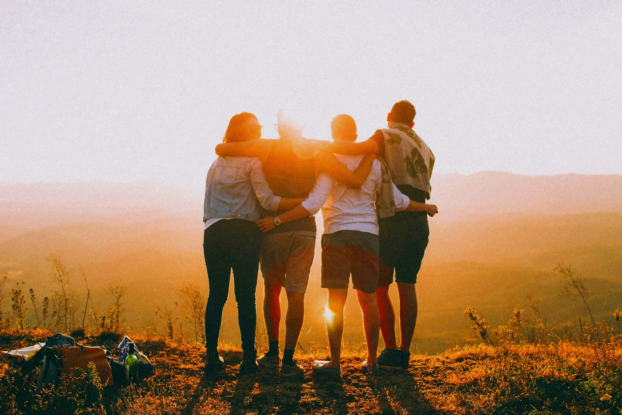 Eine Gruppe von fünf Menschen, die Hand in Hand im Sonnenuntergang die Kamera schauen, auf einer Anhöhe mit Rucksack und Ausrüstung.