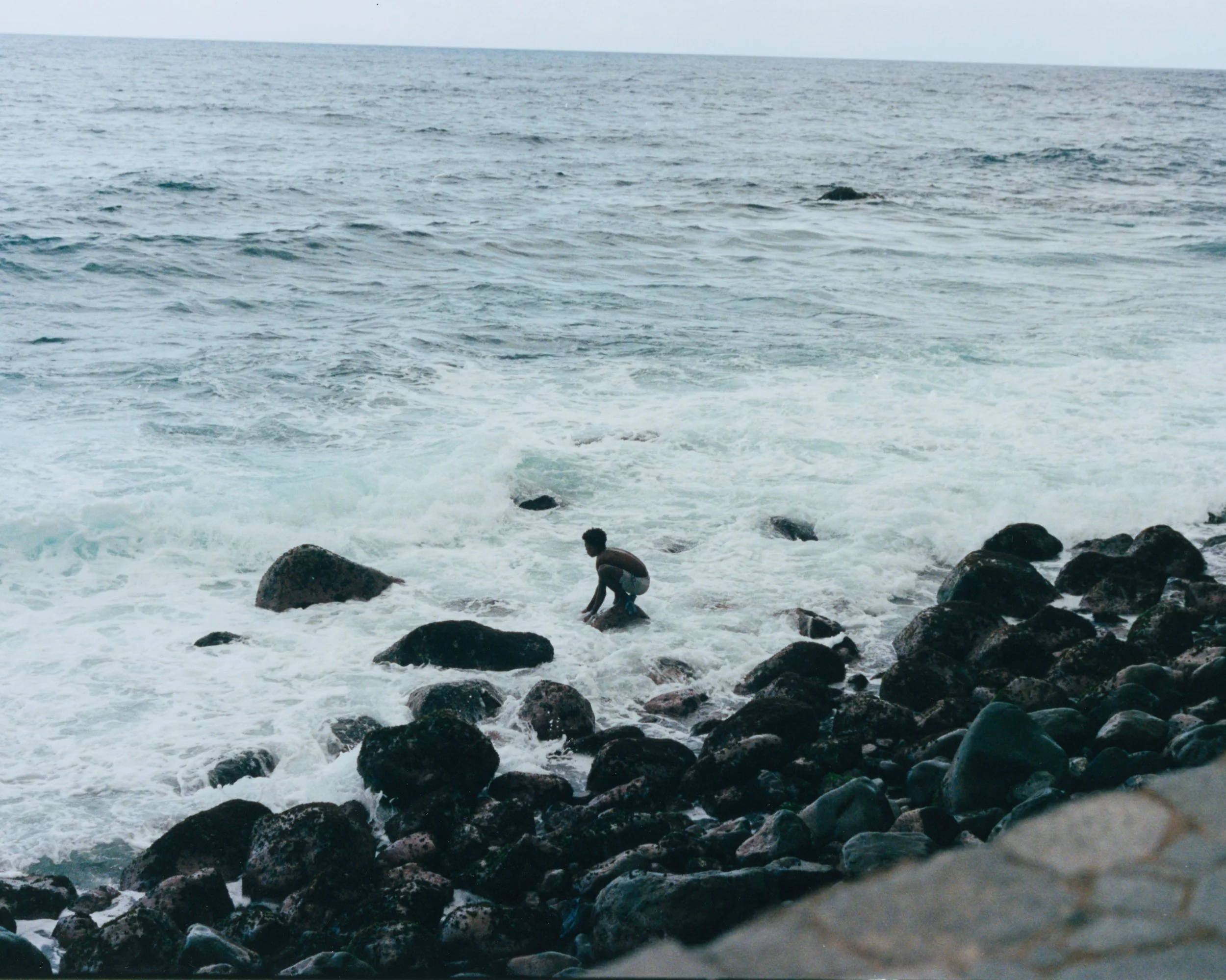 Un garçon jouant dans la mer près de la plage rocheuse.
