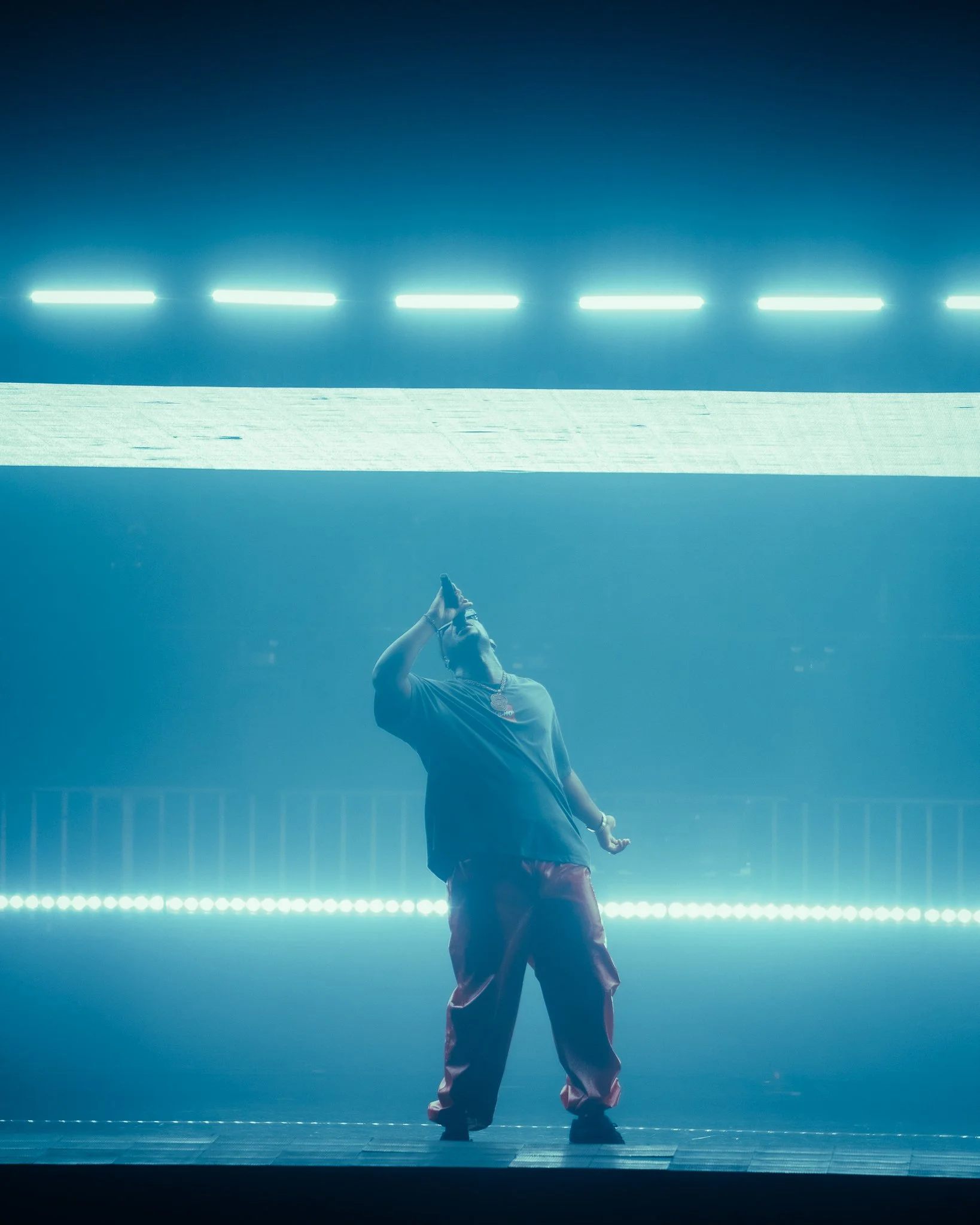 Un homme chantant sur scène sous un éclairage bleu avec des néons appuyés au plafond.