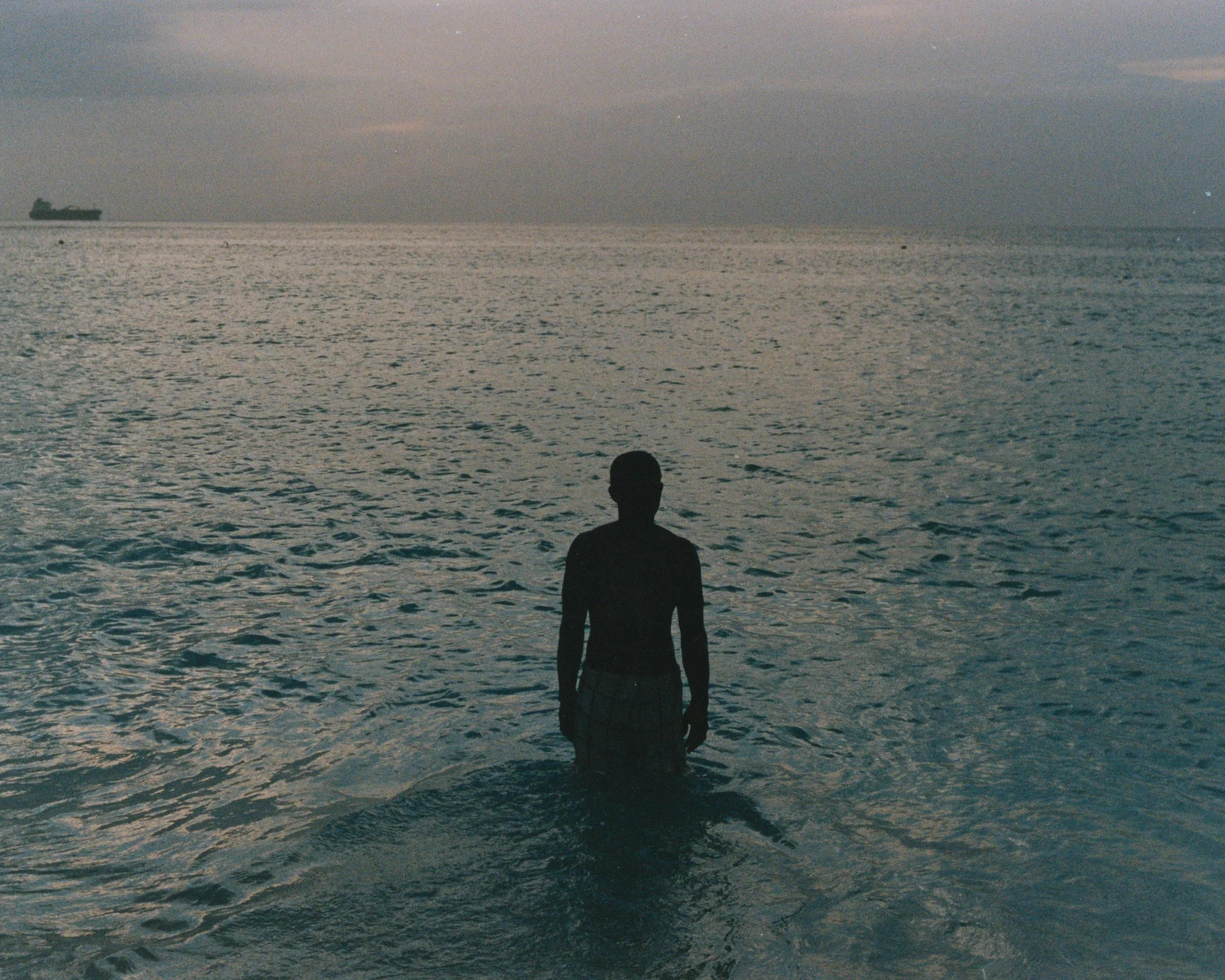 Silhouette d'un homme nageant dans la mer lors du coucher du soleil, avec un navire en arrière-plan.