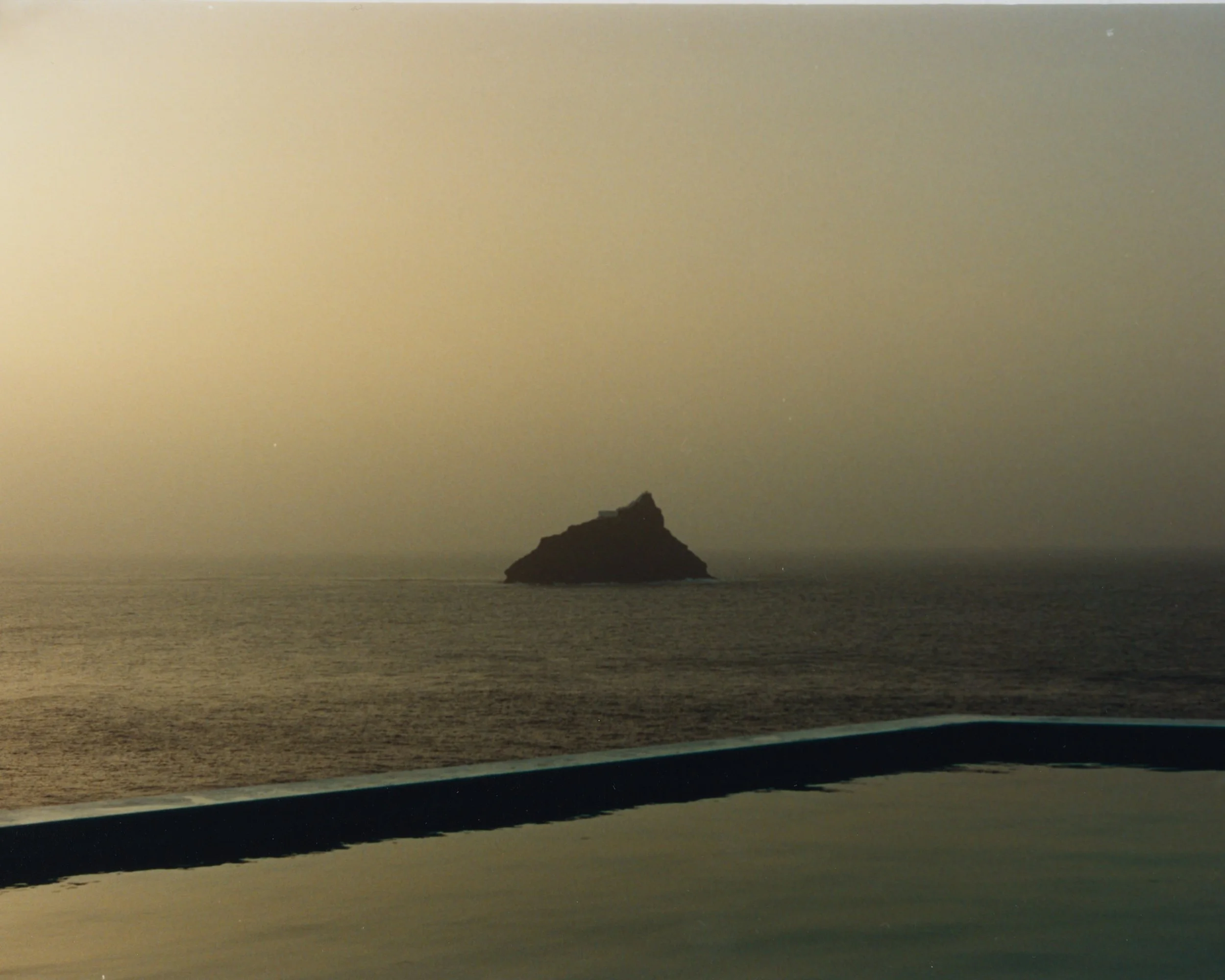 Une vue de la mer avec une roche isolée à l'horizon, le ciel semble en fin de journée ou au lever du soleil.
