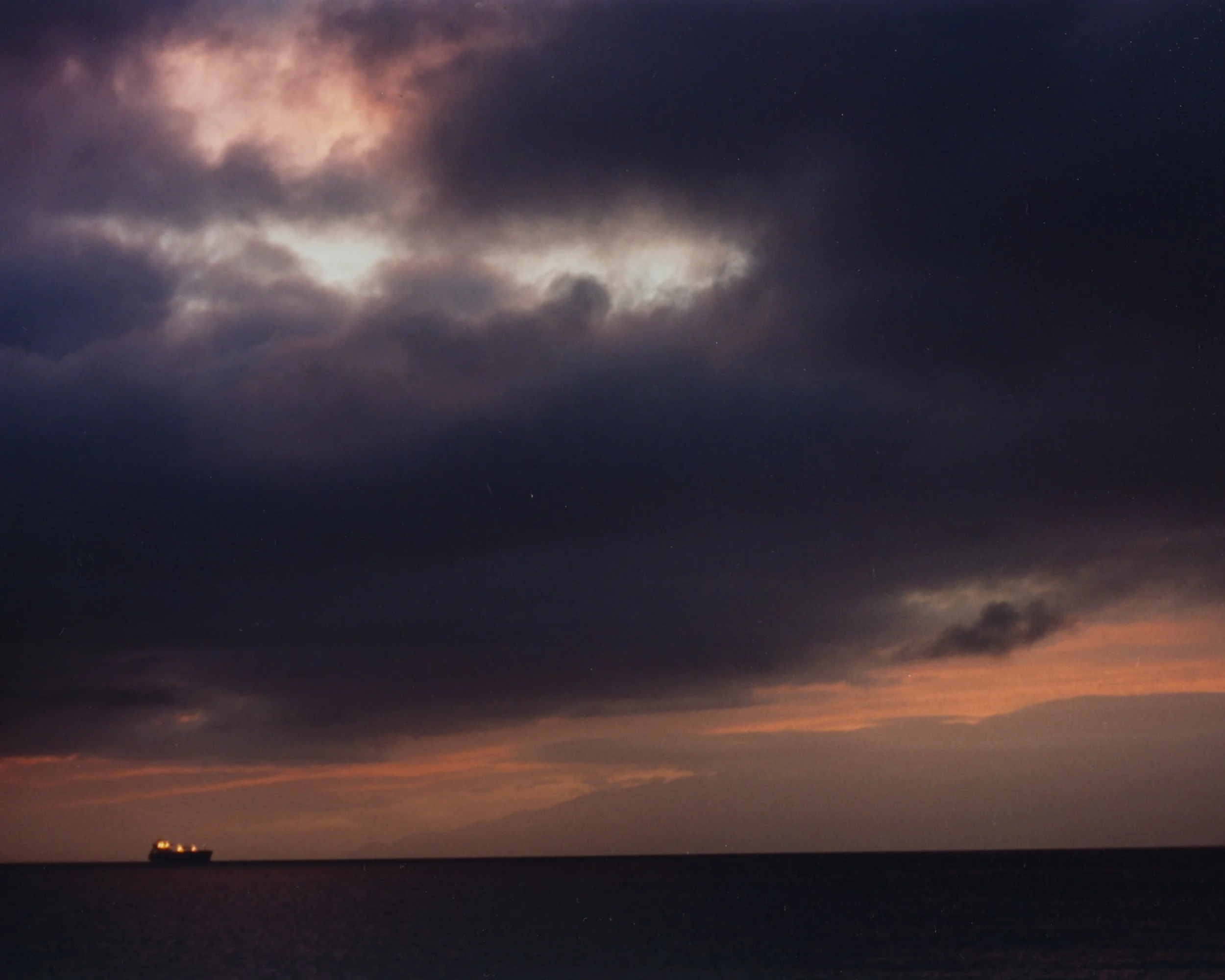 Ciel orageux avec des nuages sombres et un bateau de croisière au loin sur la mer au coucher du soleil.