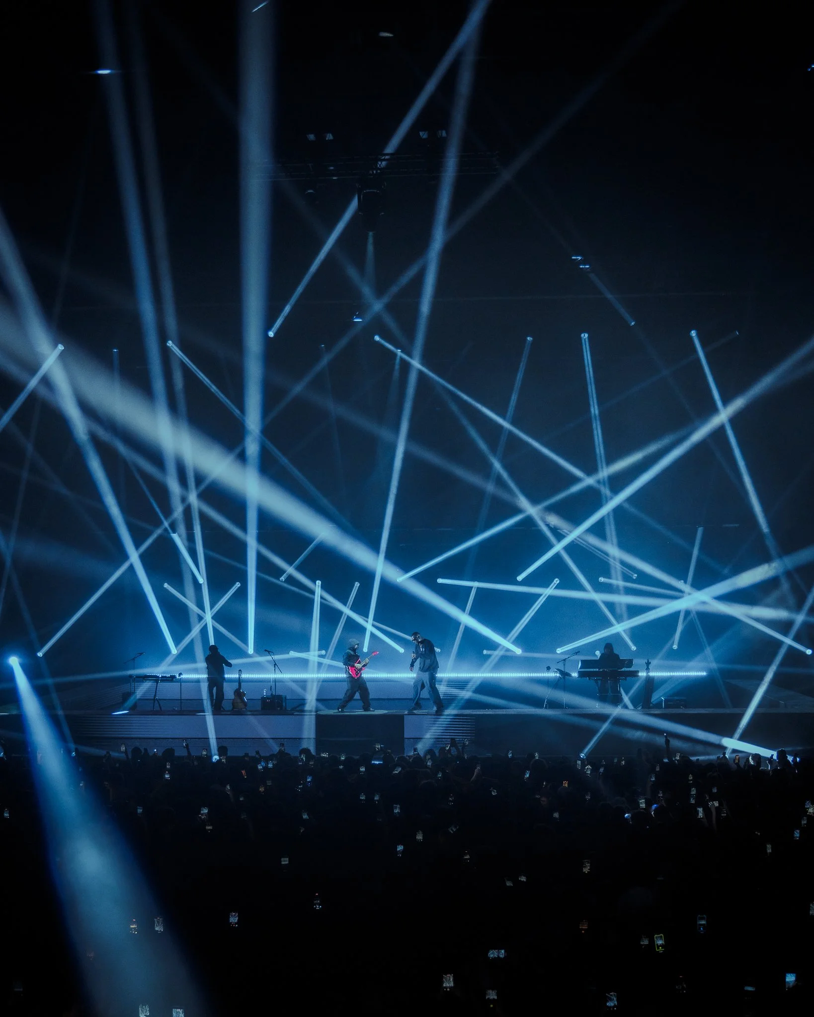 Une scène de concert avec des musiciens sur scène et un spectacle de lumières avec des faisceaux de lumière bleue et blanche.