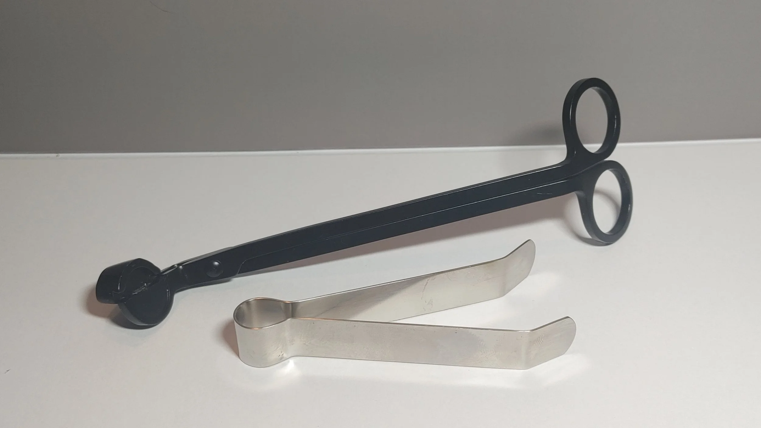 A black wick trimmer and a silver wick snuffer on a white surface. Links to accessories.