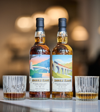 Two bottles of James Eadie whiskey and two glasses of whiskey on a bar counter with blurred lights in the background.