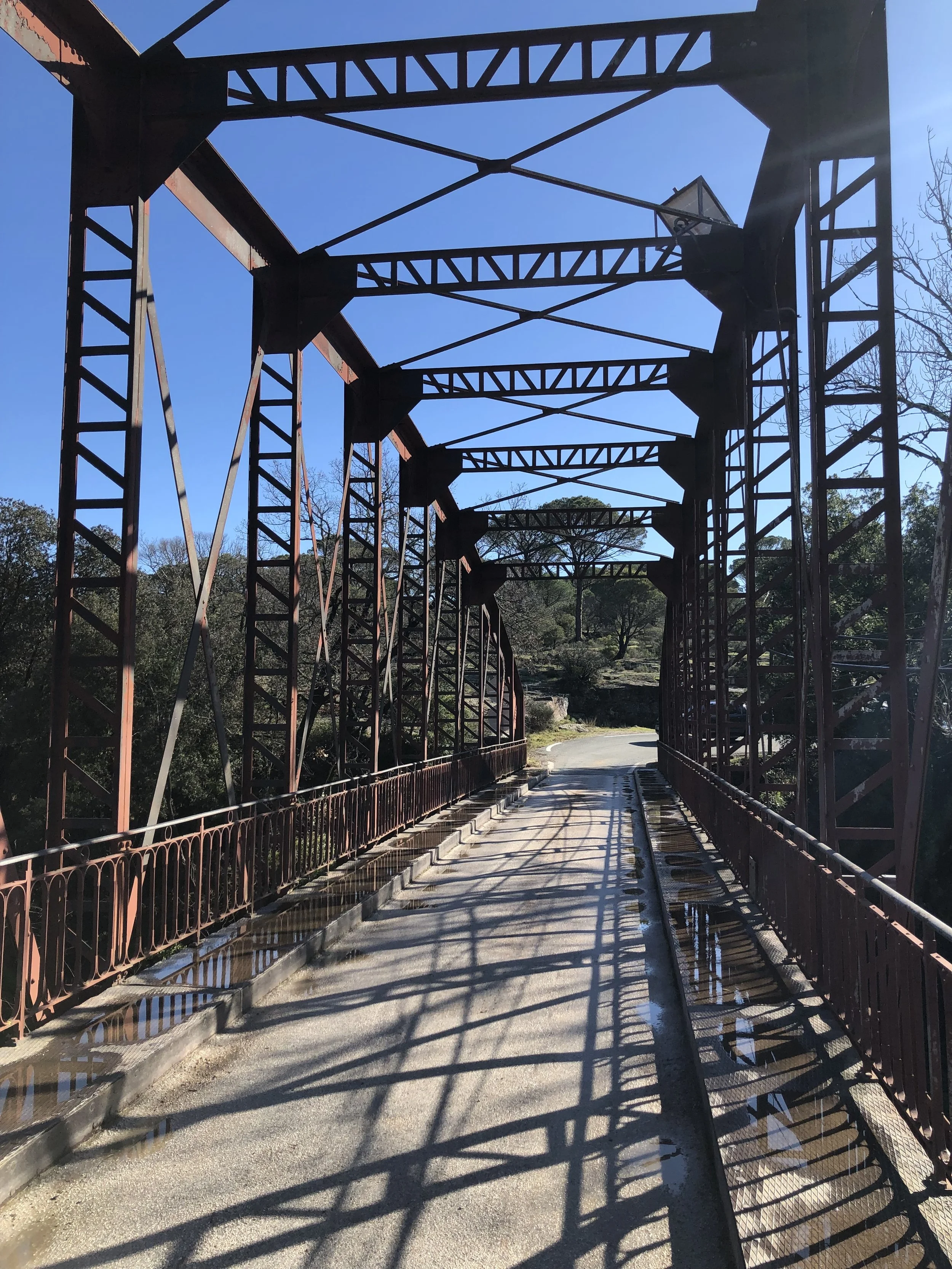 Pont en fer avec structure en treillis en fer et garde-corps en fer forgé, en plein jour avec ciel bleu et ombres du pont sur la chaussée