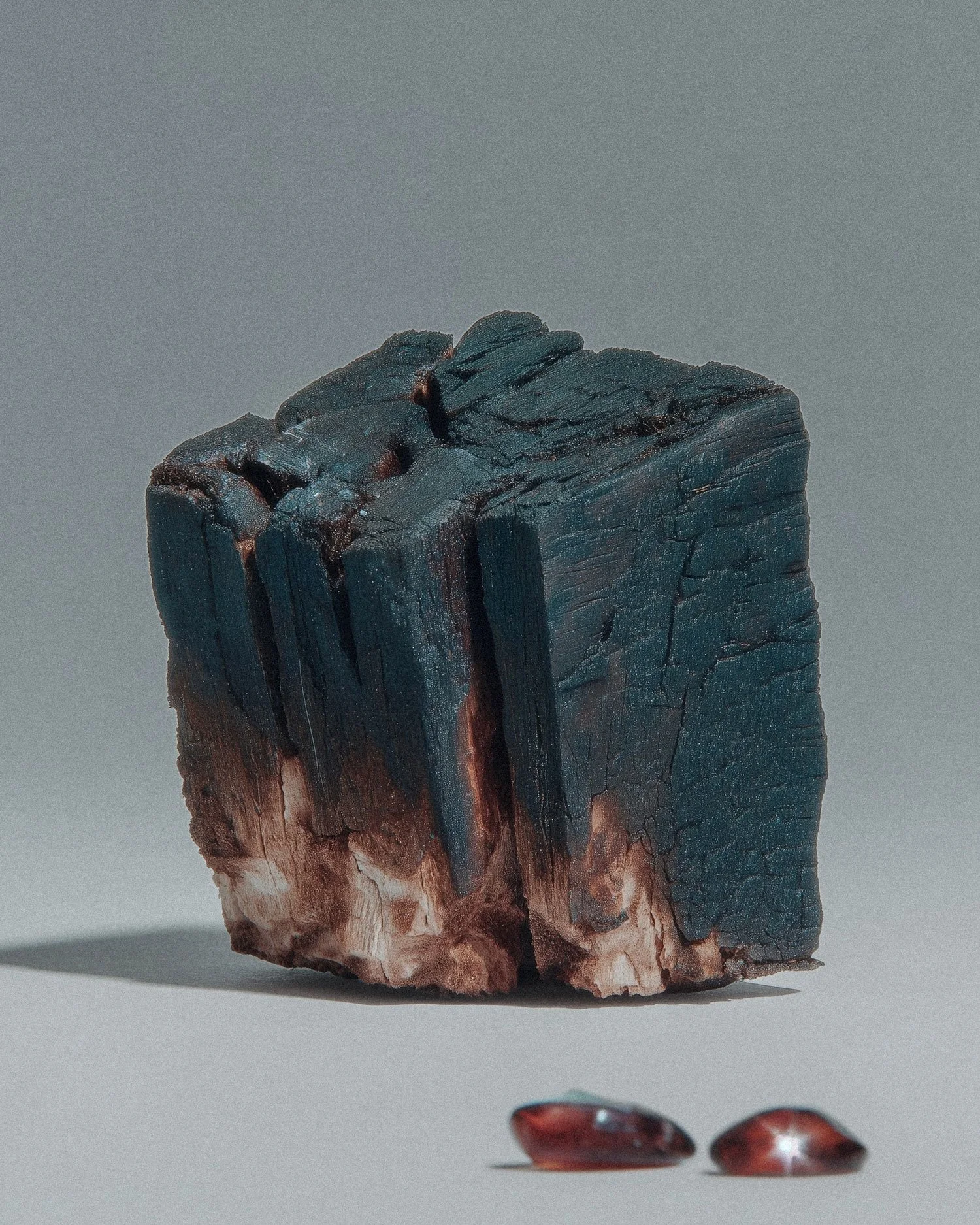 A large piece of black and brown meteorite with a rough, cracked surface, placed on a plain background with two smaller polished stones nearby.