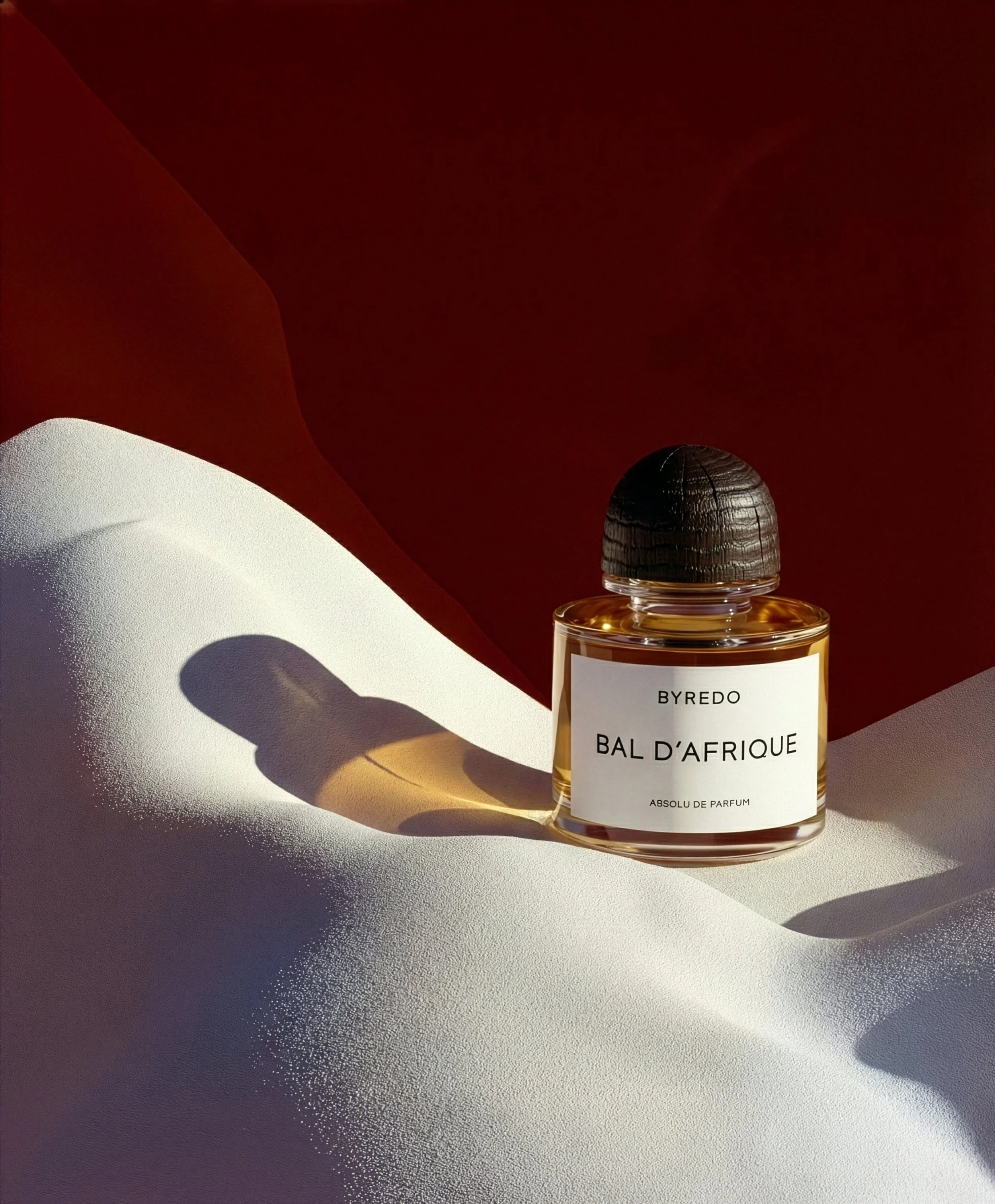 Perfume bottle labeled 'Bal d’Afrique' by Byredo on a textured white surface with dramatic lighting and shadows.
