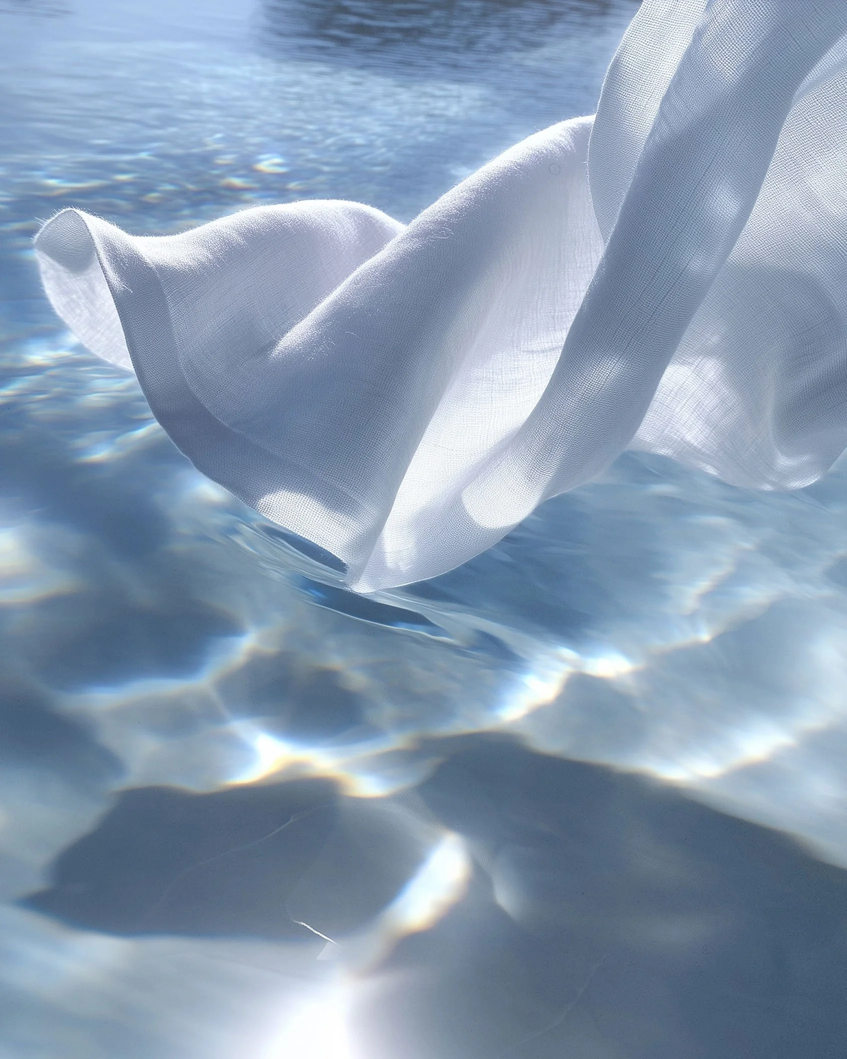 A white, semi-transparent fabric floating on water with sunlight reflecting off the surface.