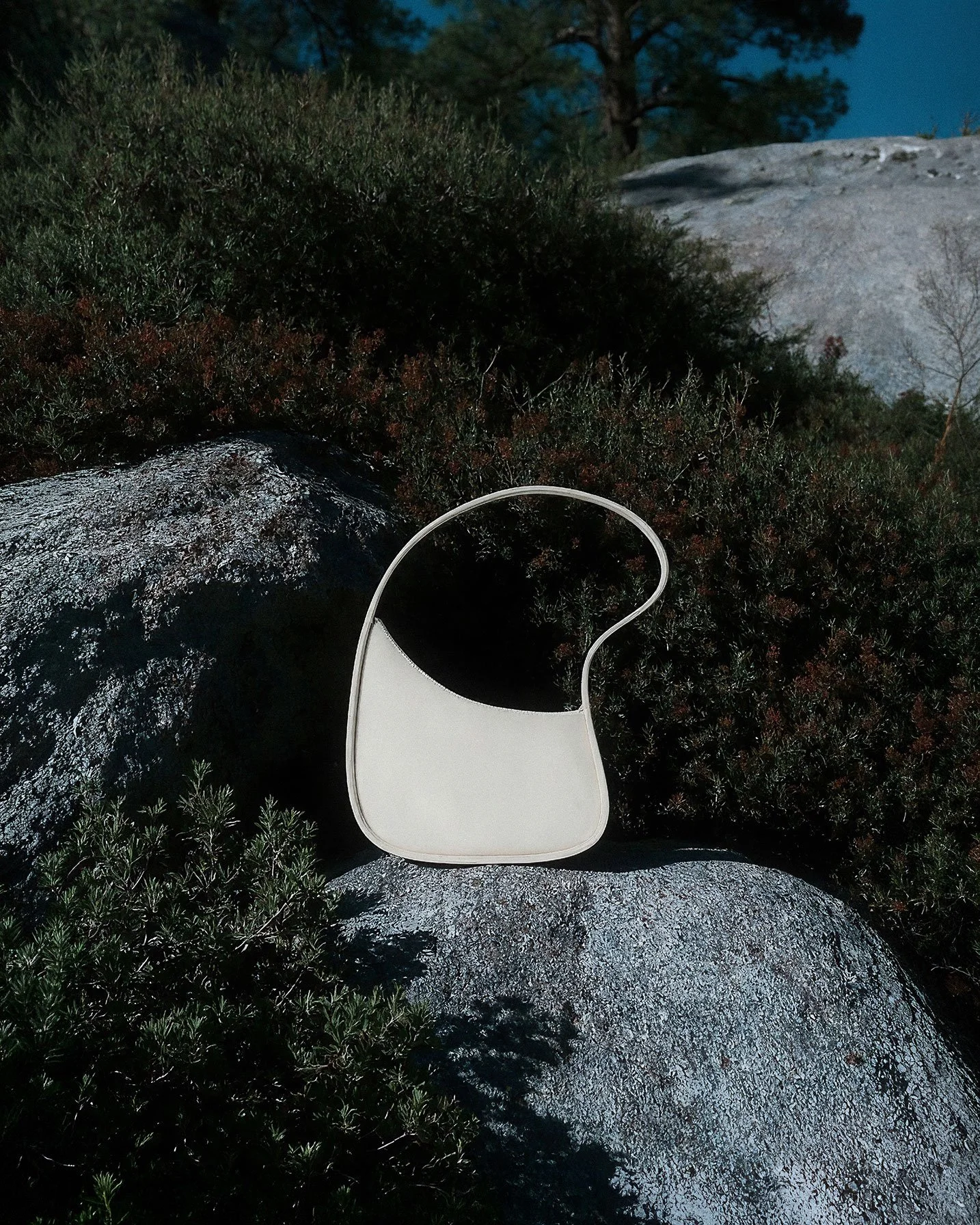A white face mask resting on a large rock outdoors surrounded by green bushes and trees.