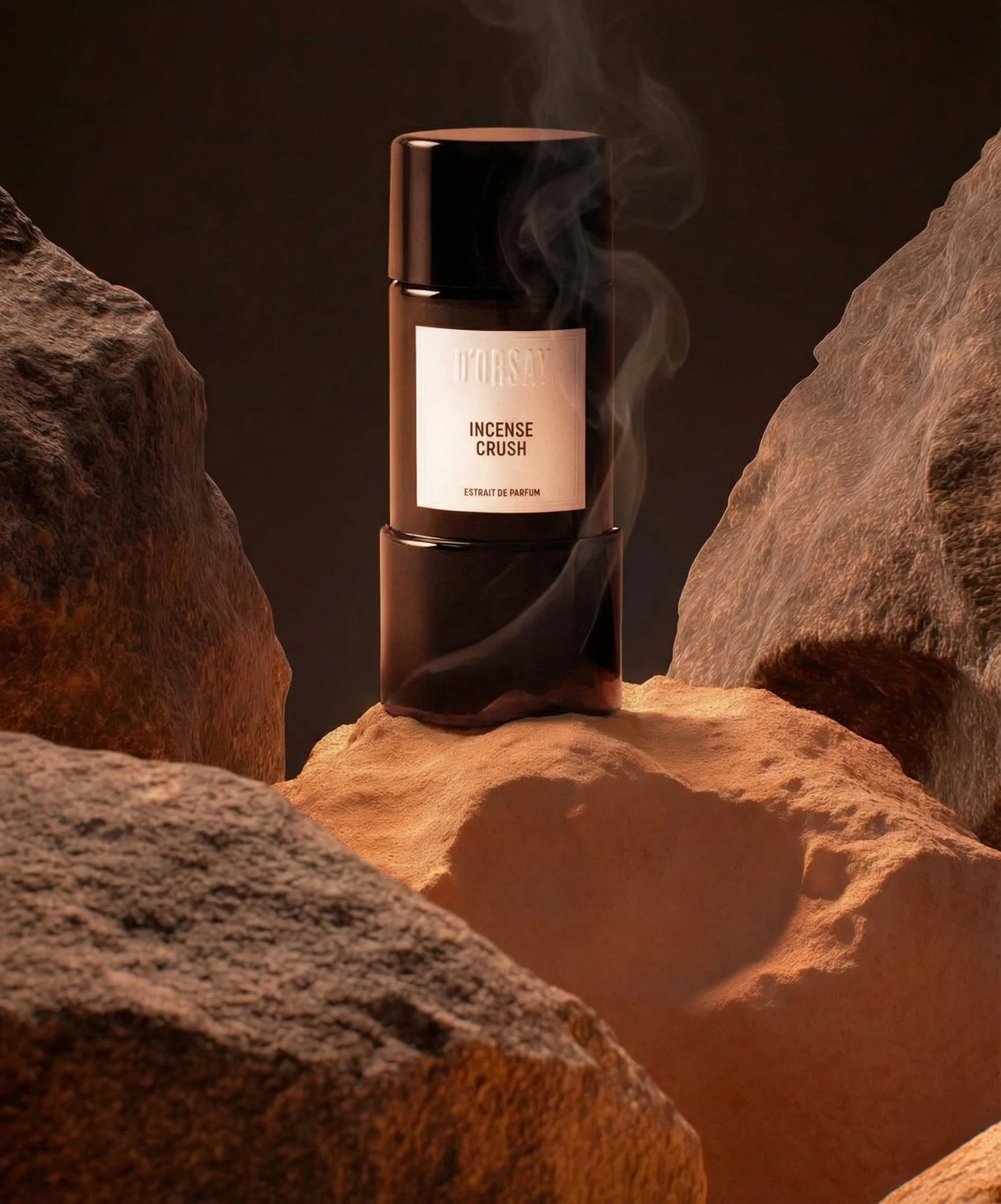 A black cylindrical container with a white label reading 'Incense Crush' and 'Estrat de Parfum' is placed on a rock amidst other rocks, with wisps of smoke rising from the container against a dark background.