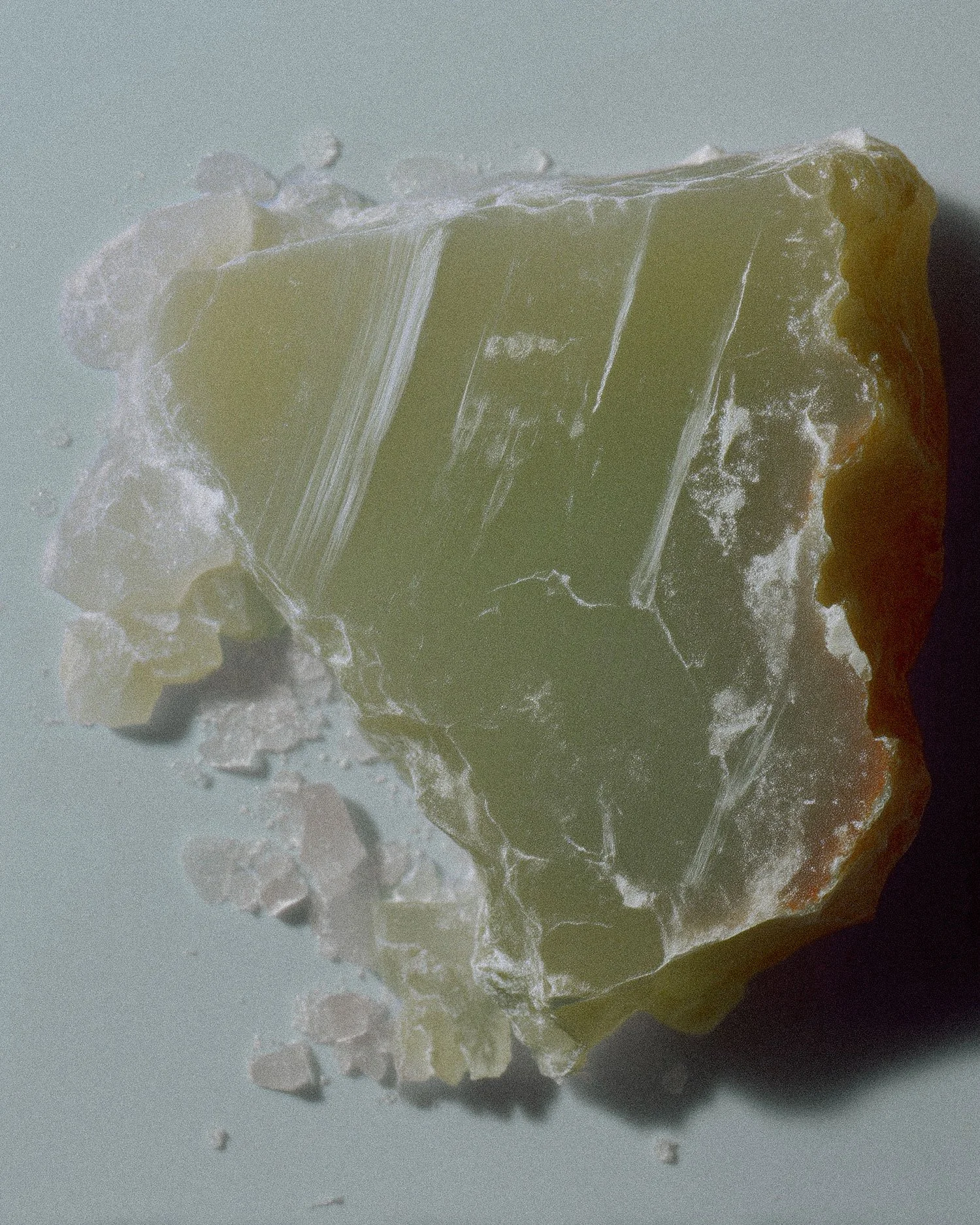 Close-up of a partially broken piece of yellowish-green soap with smaller soap scraps on a light background.