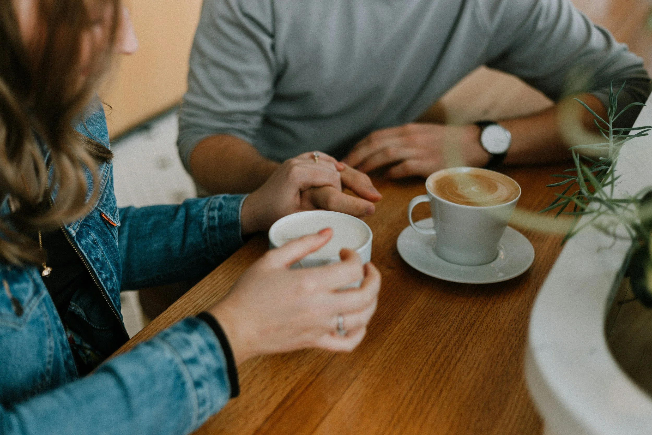 Two people holding hands and drinking coffee at a wooden table reflecting on their Christian counseling session for relationship stress and setting boundaries
