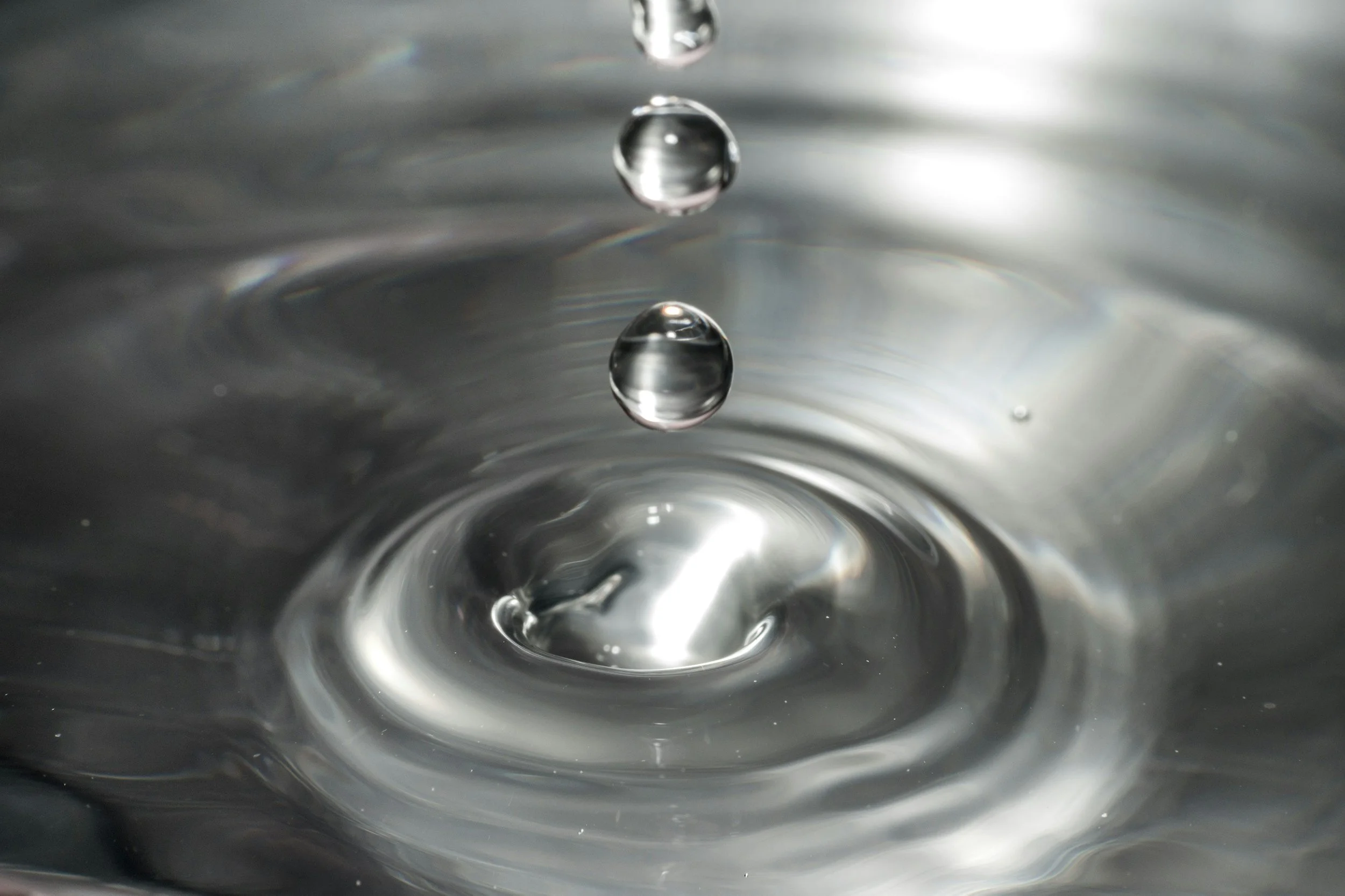 Close-up of water droplets splashing into a liquid surface, creating a ripple effect.