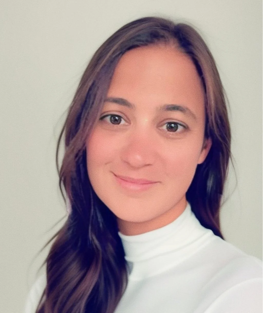 Woman with long brown hair wearing a white turtleneck, smiling.