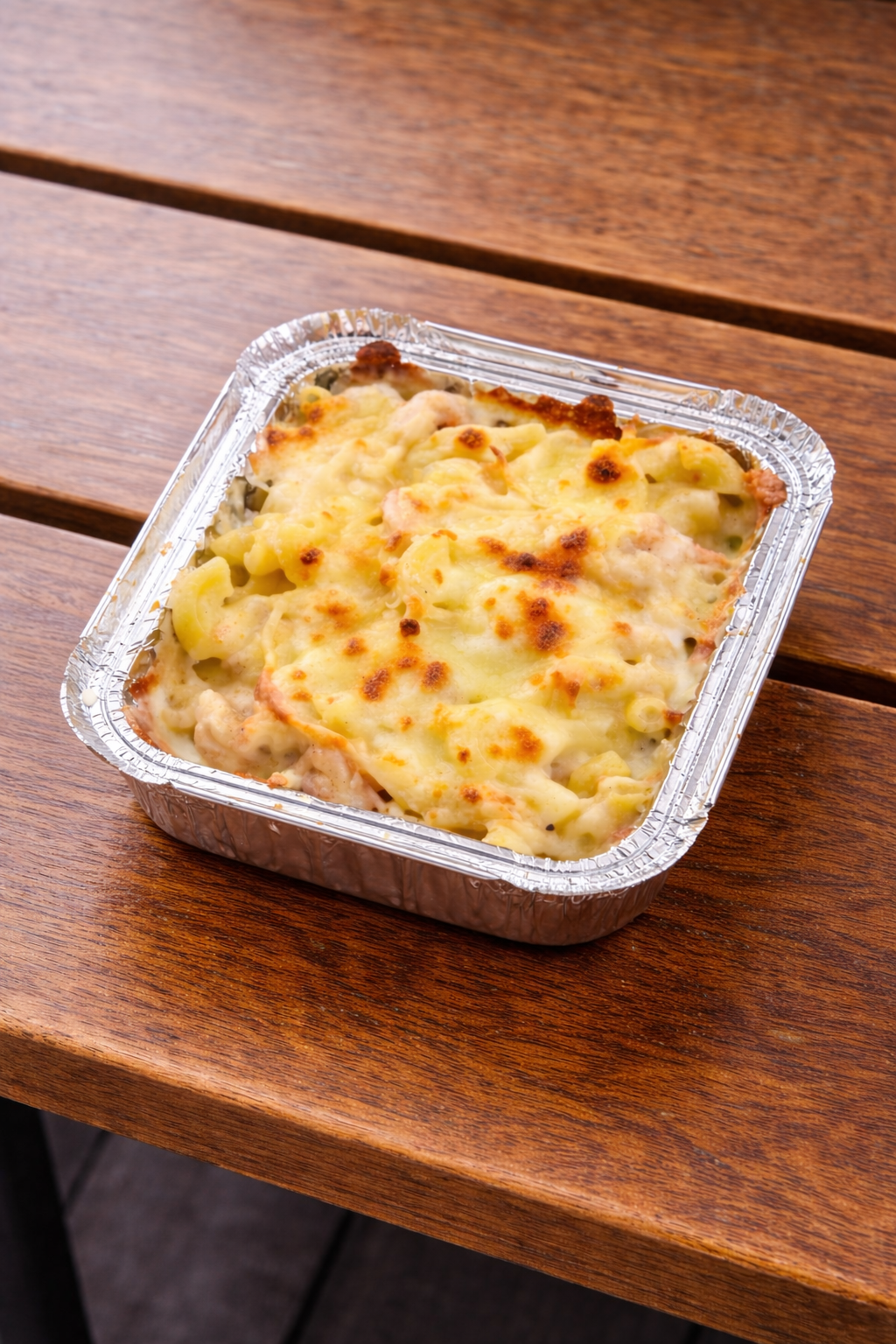 Baked macaroni and cheese in an aluminum foil container on a wooden table.