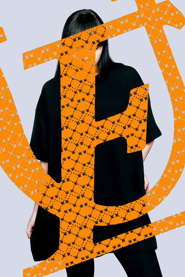 A person with long black hair wearing a black shirt and pants, standing against a plain light gray background, partially obscured by an orange overlay with small black designs.