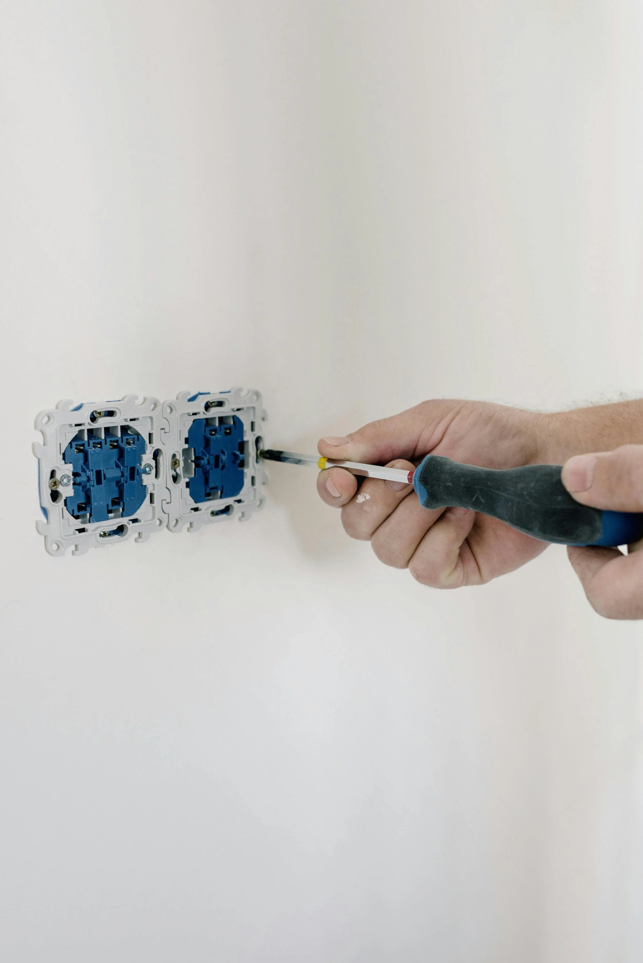 A person installing electrical outlets into a wall with a screwdriver.