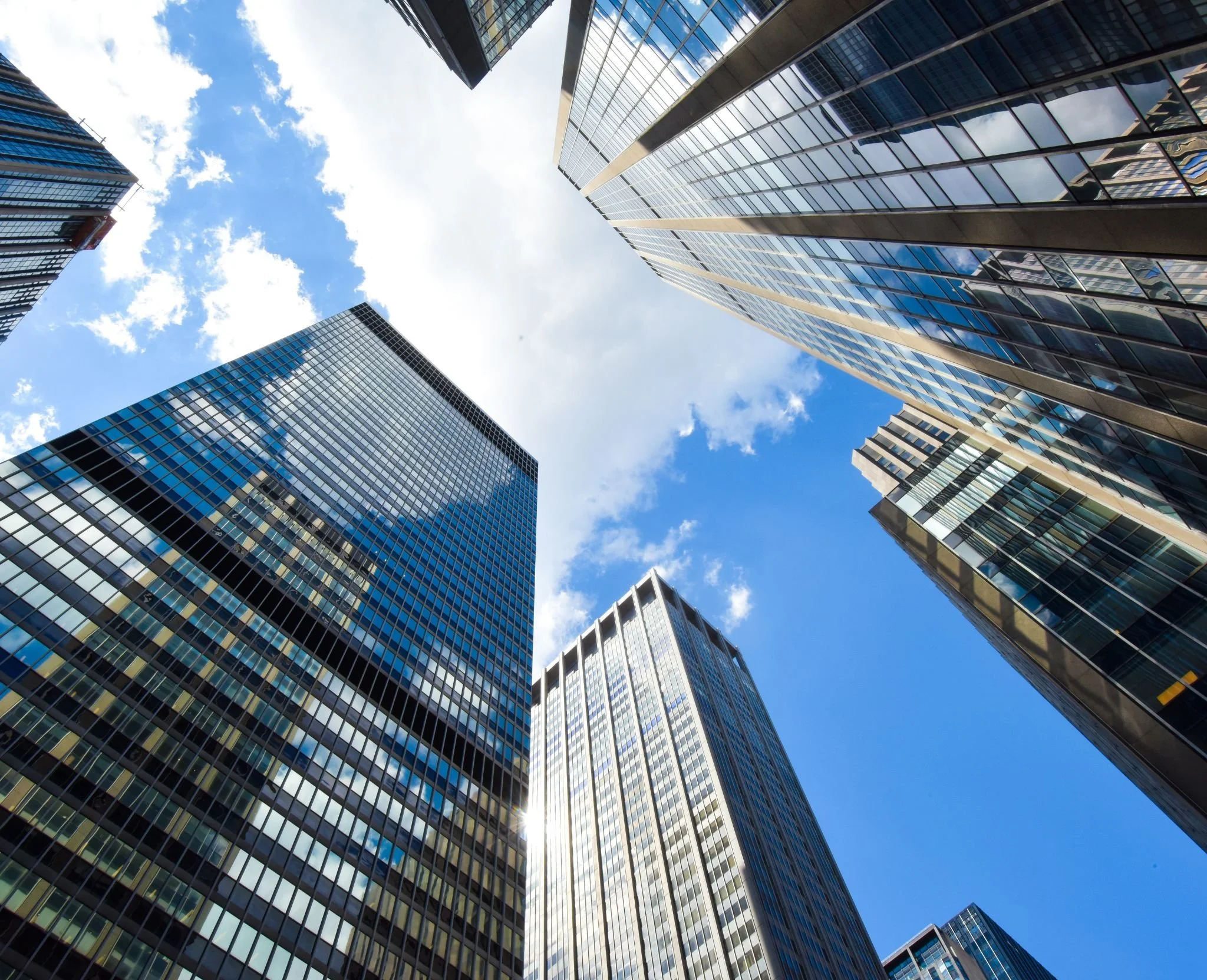 Looking up at skyscrapers in a city with a bright blue sky and some clouds.