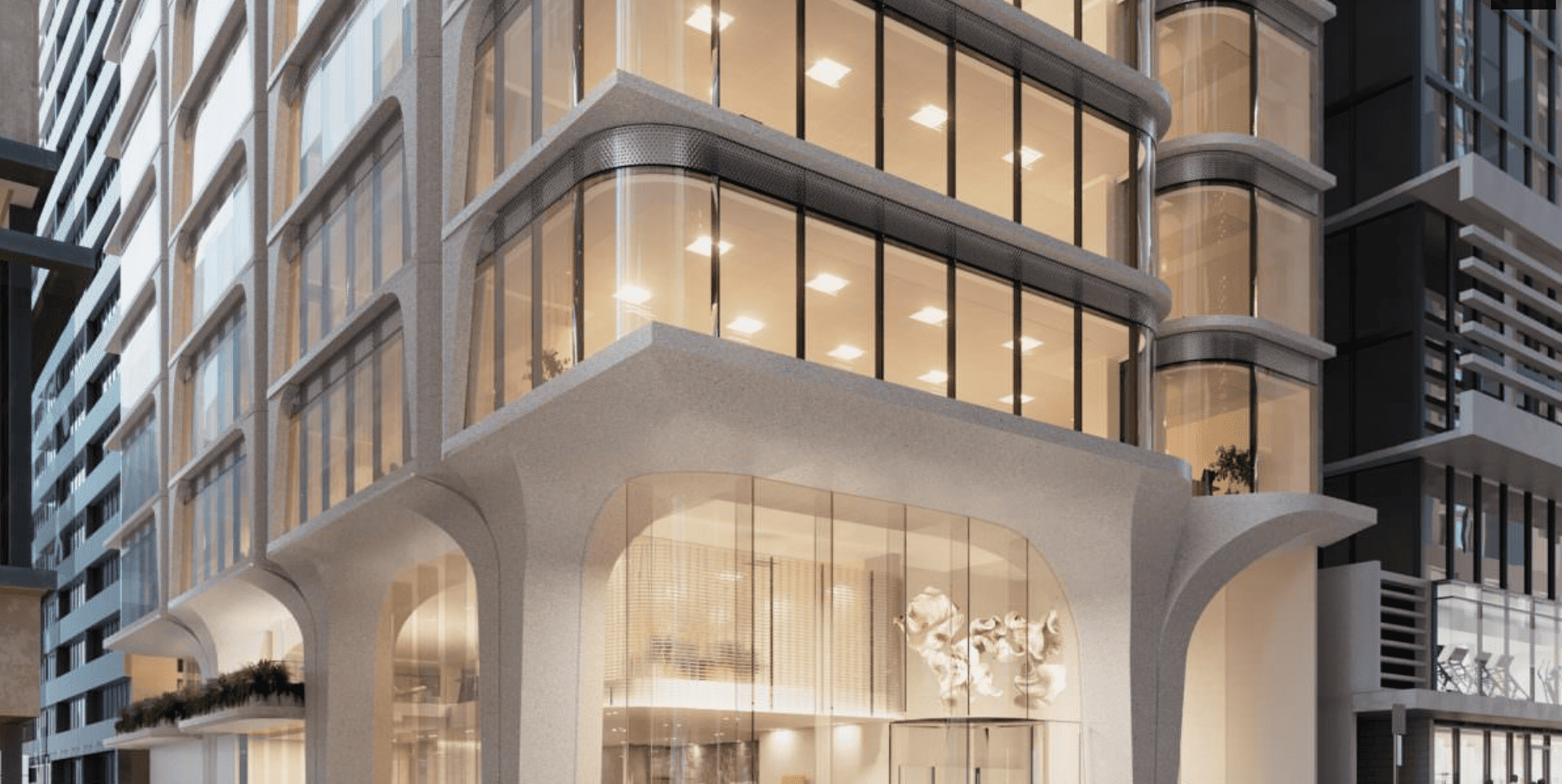 Modern multi-story building with large glass windows and curved architectural design, featuring an illuminated interior on the ground floor.