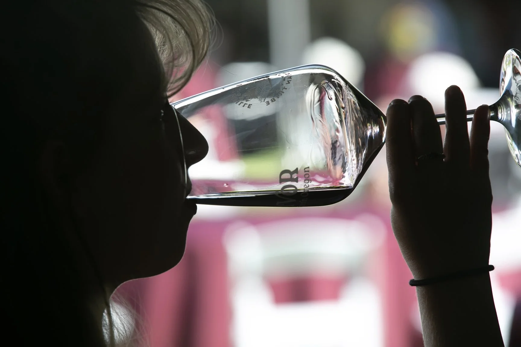 Person drinking from a clear wine glass with black wine, with a blurred background.