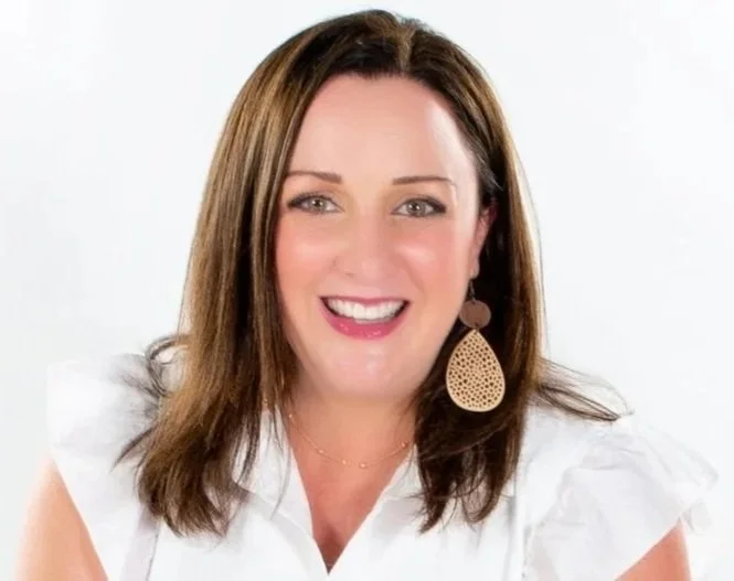Smiling woman with shoulder-length brown hair, wearing large drop earrings and a white blouse.