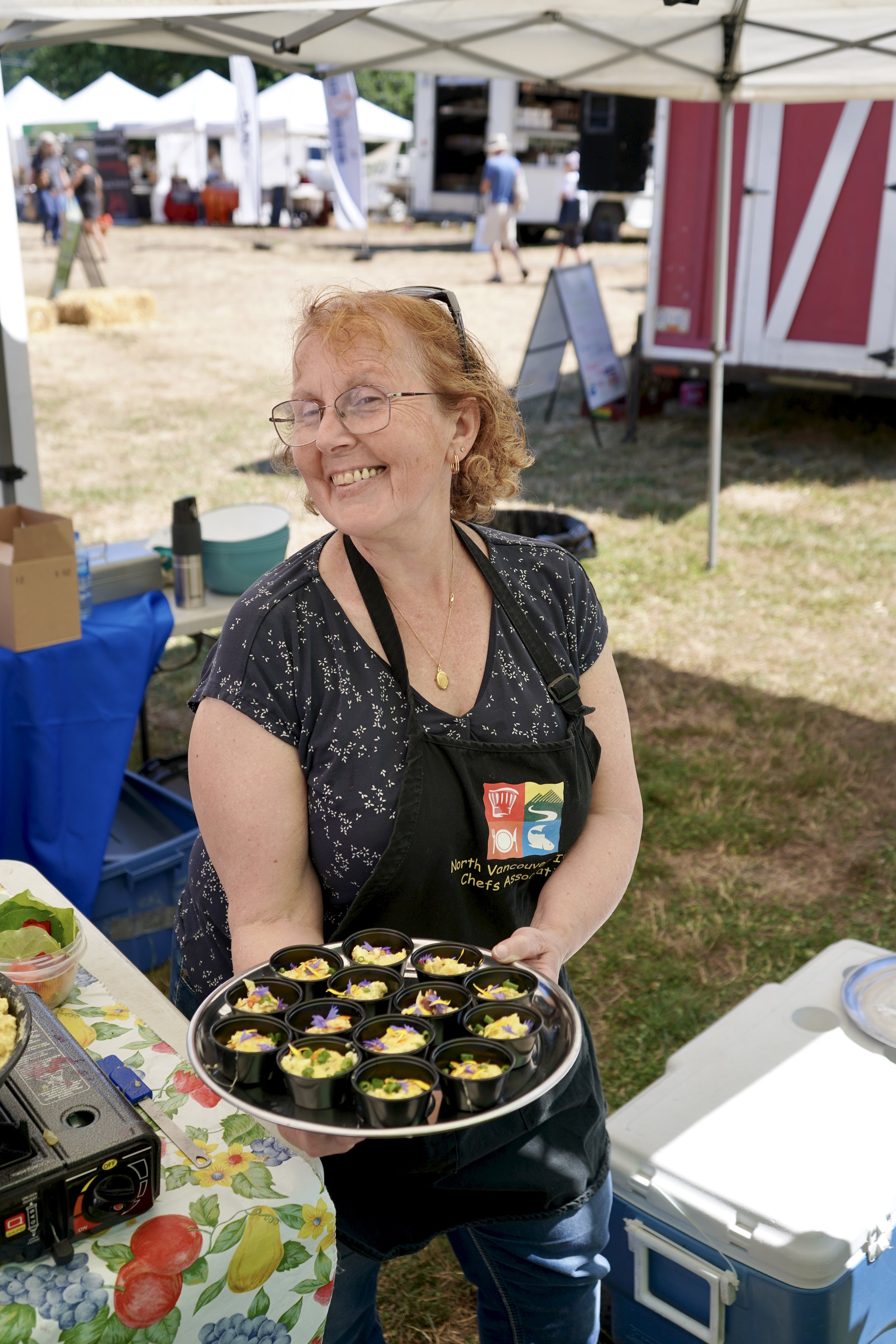 Smiling woman with glasses and curly red hair, wearing a dark jacket and striped shirt.