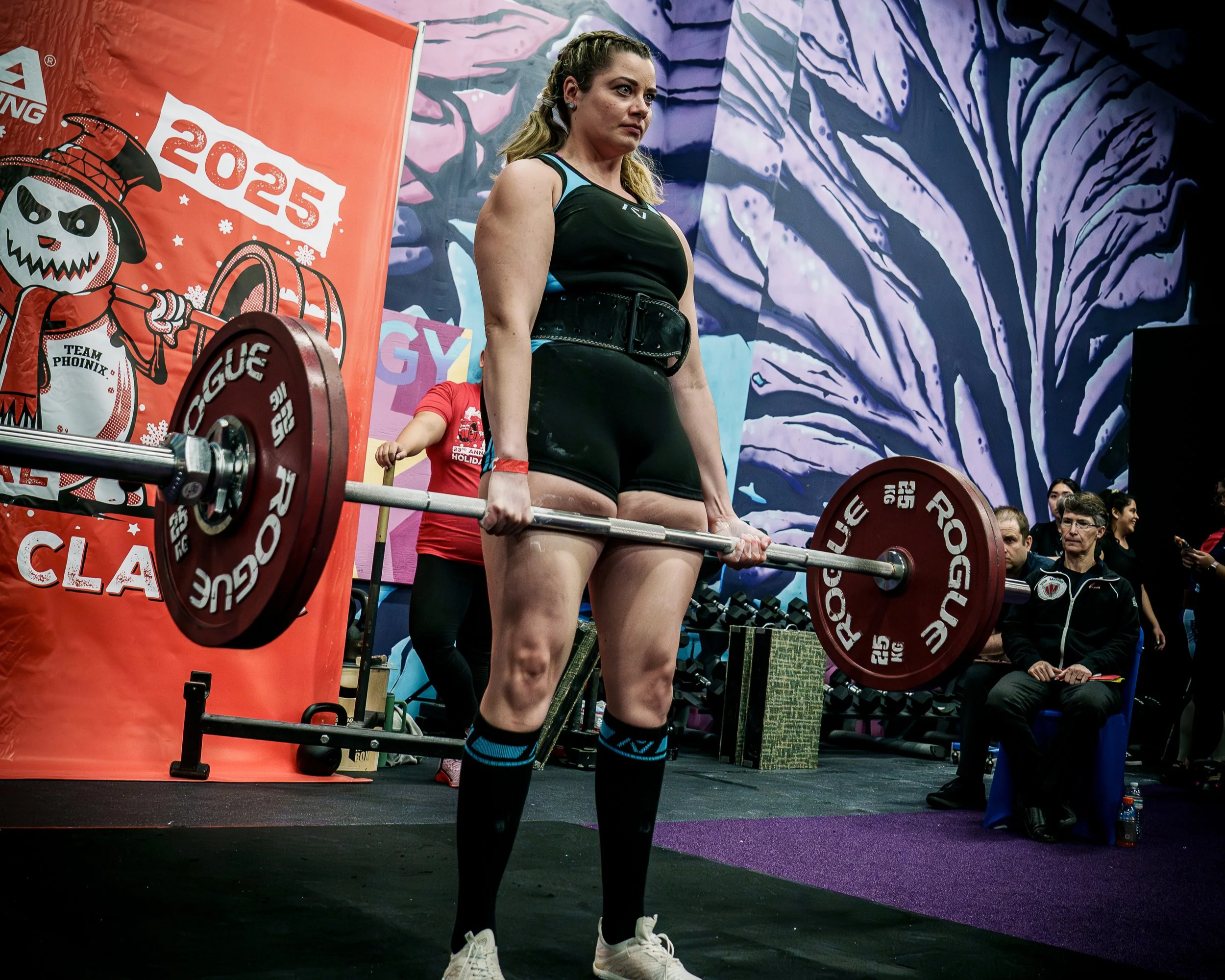 A woman lifting a barbell during a powerlifting competition, with people and colorful backgrounds observing.