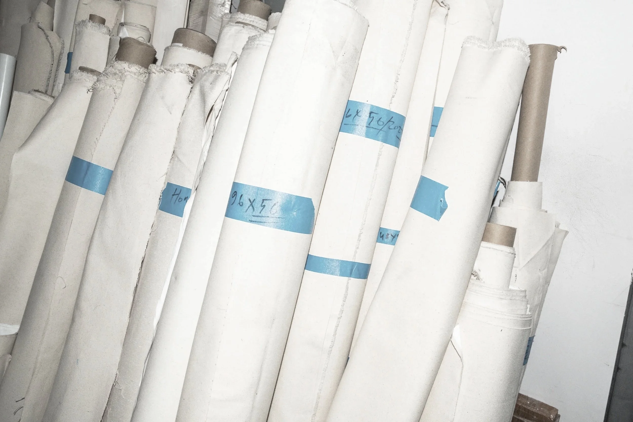 Mehrere liegende große Papierrollen mit blauen Beschriftungsstreifen stehen an einer Wand.