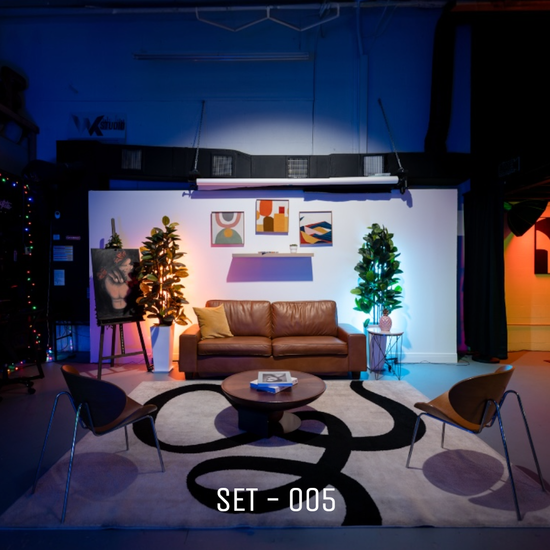 WK-Studios Set 005 is a modern lounge-style set built for interviews, podcasts, and lifestyle content. Featuring a brown leather sofa, sculptural chairs, and a bold abstract rug, the space blends warmth with contemporary design. Accented with greener