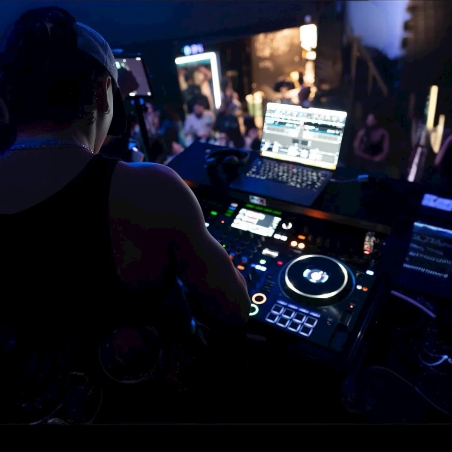 DJ mixing music at a nightclub with crowd in the background, illuminated by colorful lights.