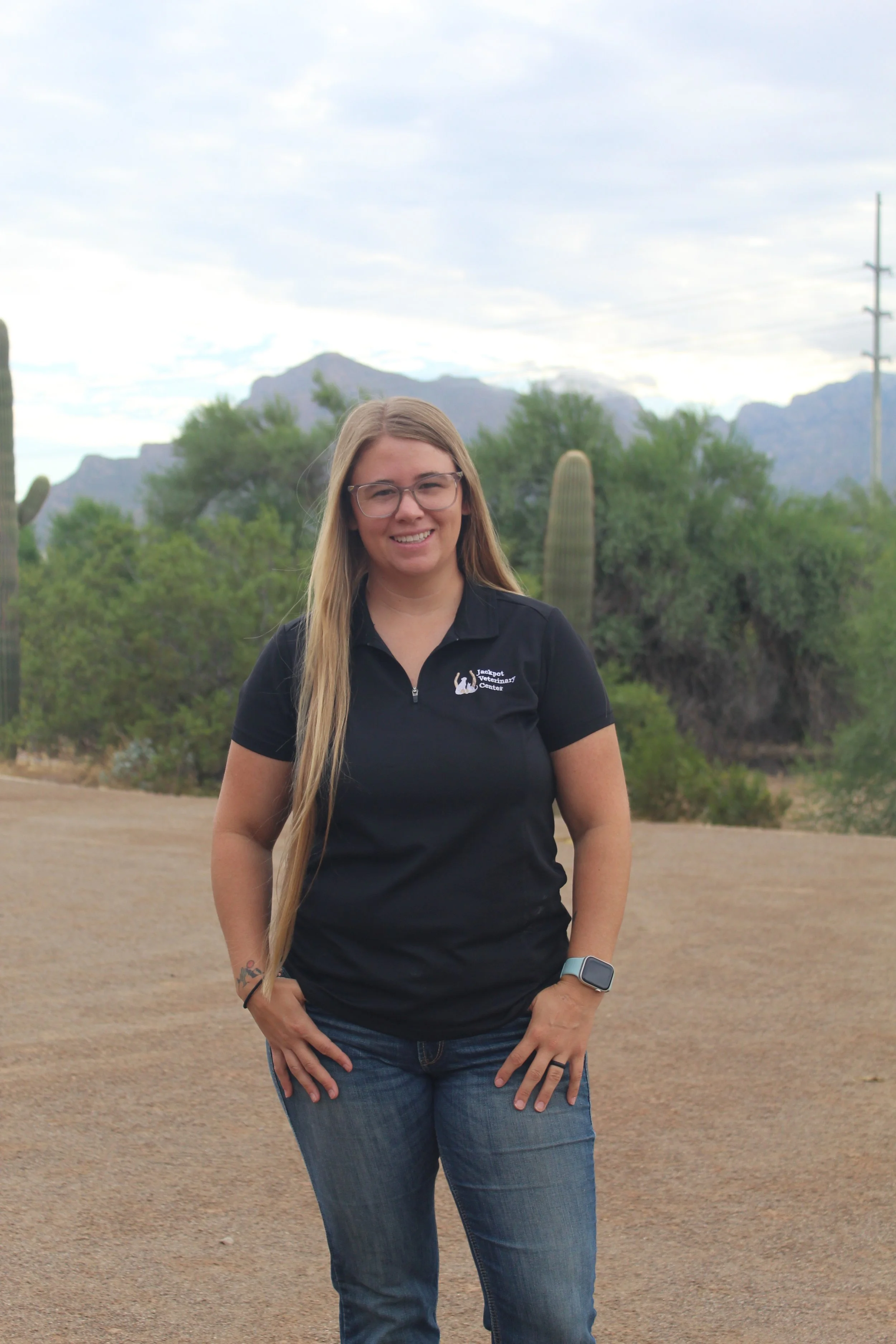 Person standing outdoors with cactus and desert background, wearing a black shirt and jeans