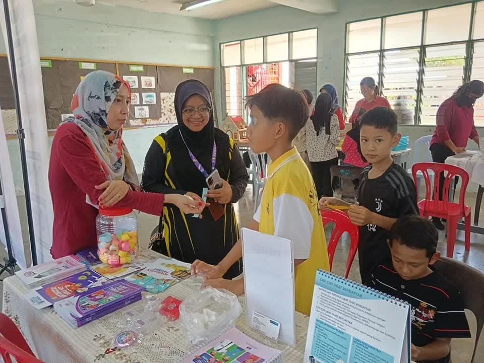 People at a table distributing colorful candies and informational brochures, with children and adults engaging in conversation.