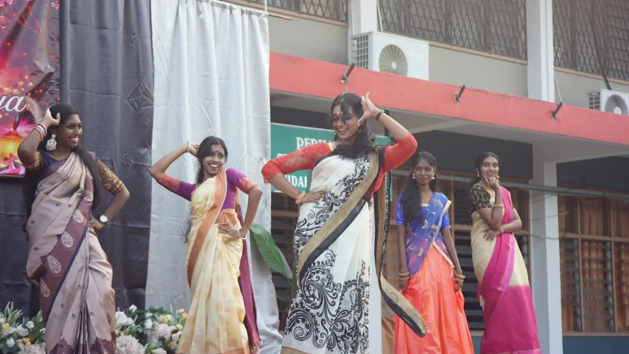 Five women in colorful traditional sarees performing a dance on stage during a cultural event.