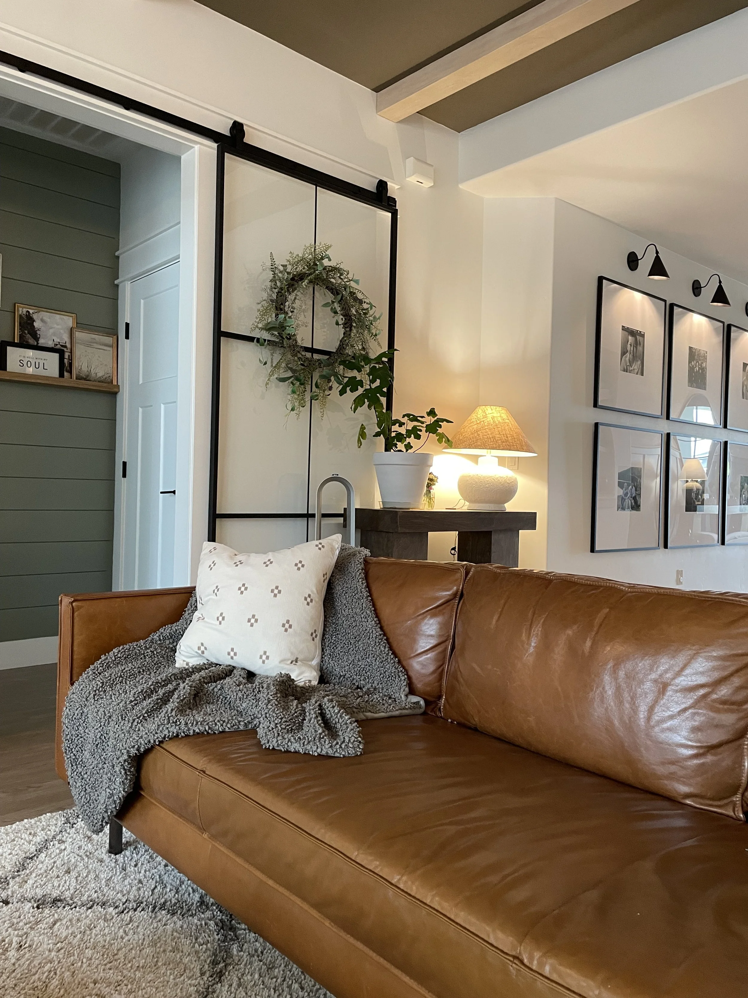 image of a living room sofa, with a throw pillow and blanket. in the background a console table with a lamp on it