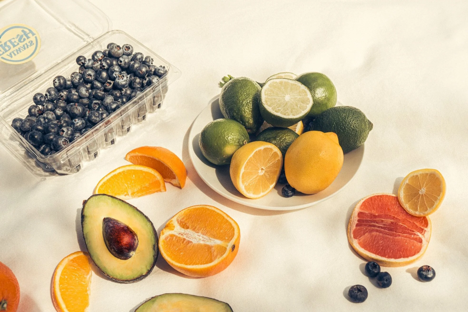Plate of lemons, limes, blueberries along with oranges, avocado, and grapefruit on picnic blanket.