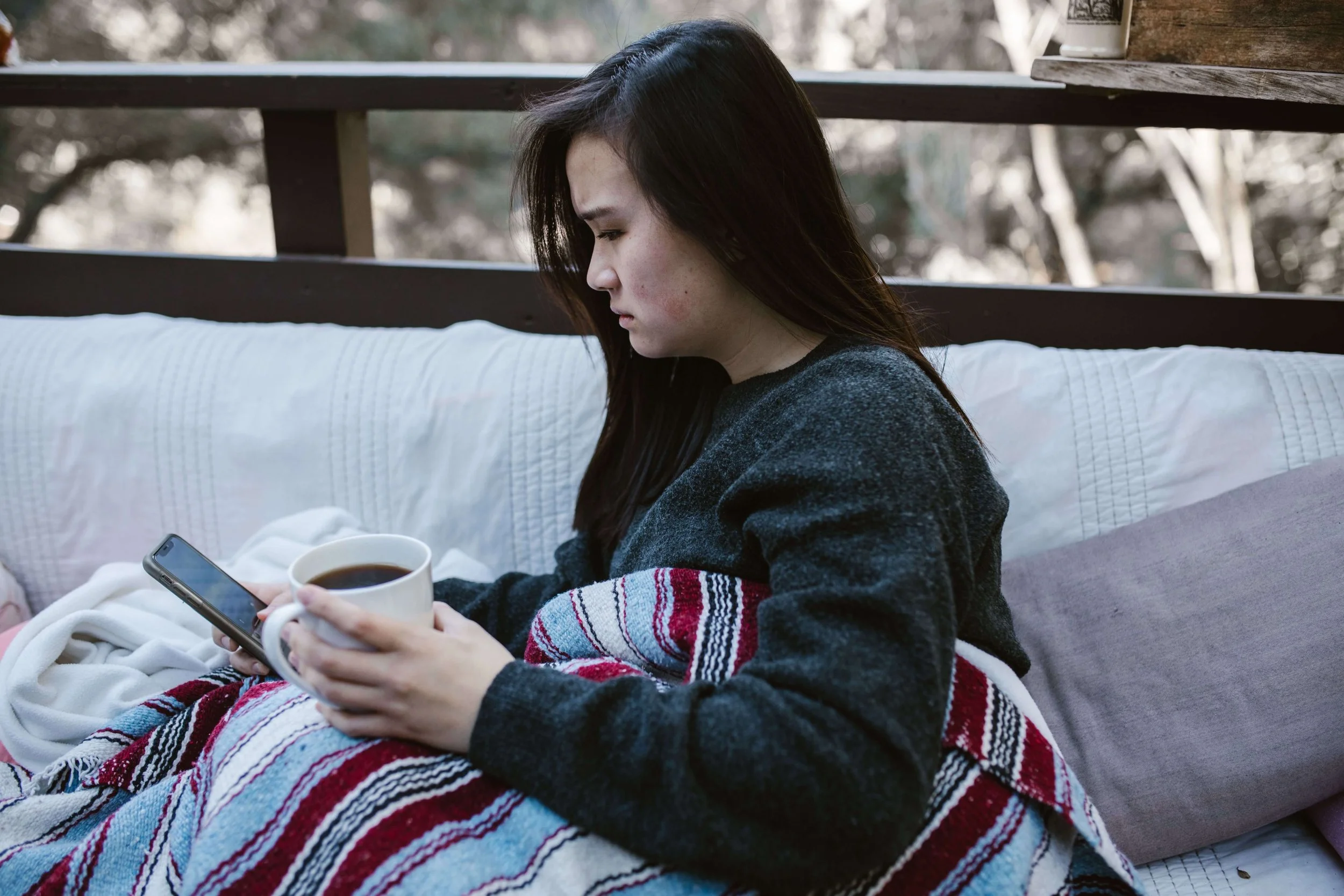 Woman sitting with a blanket and mug looking sad and thoughtful, representing the emotional impact of old attachment wounds explored through therapy for young adults in Manhattan.