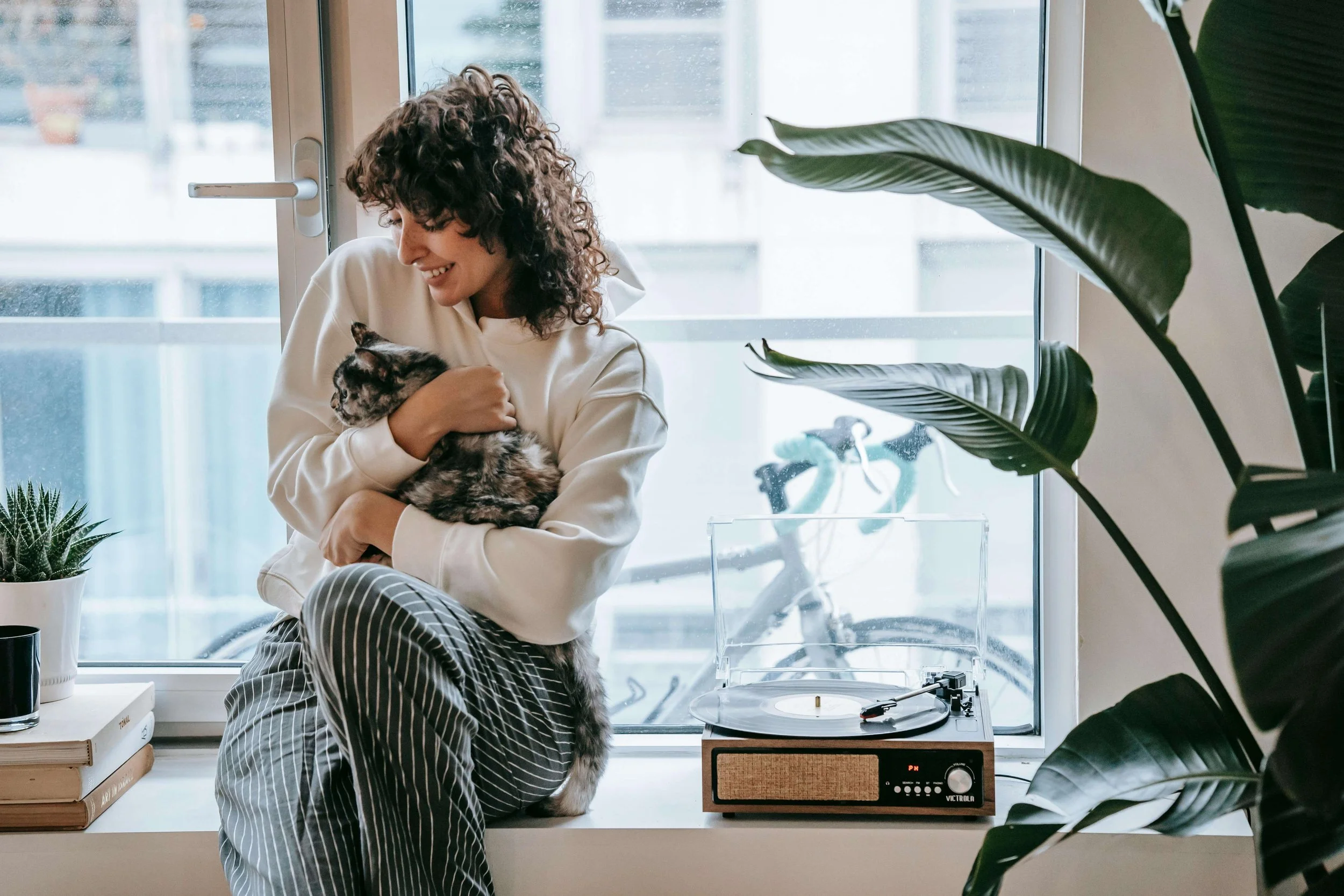 Young adult holding a cat by a window in a quiet home setting, representing comfort, regulation, and emotional support in anxiety therapy for young adults in Manhattan.